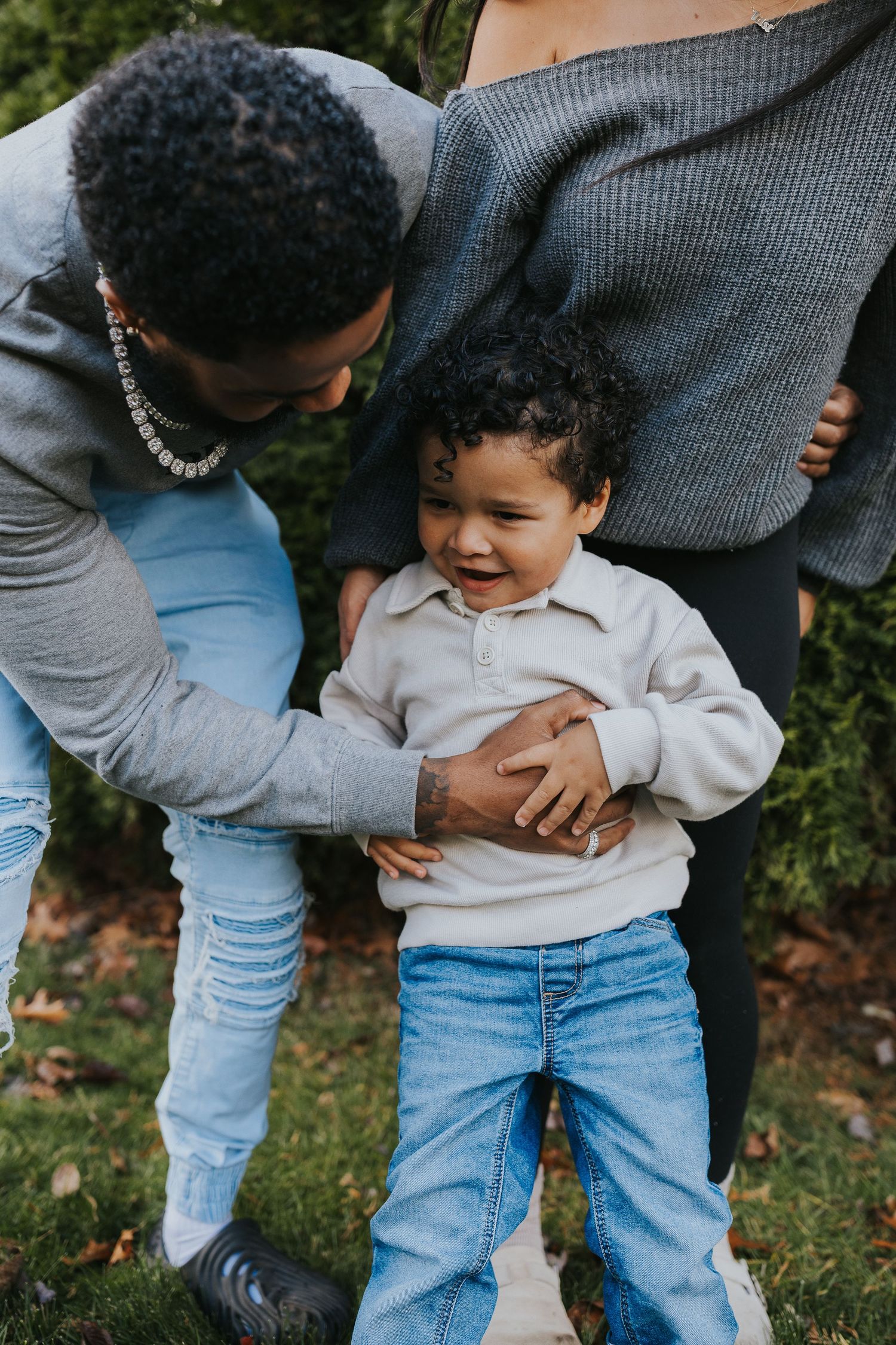 Family moment with parents playing with their laughing toddler son in an outdoor garden.