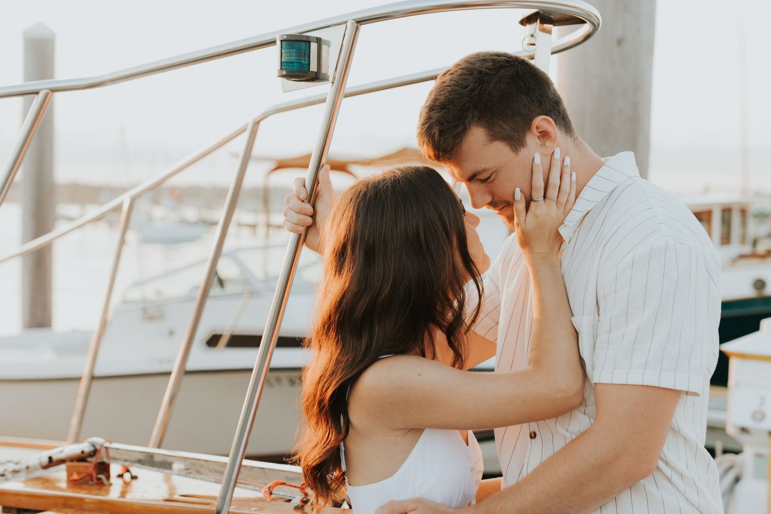Couple sharing a tender almost-kiss moment on a sailboat at a sunny marina.