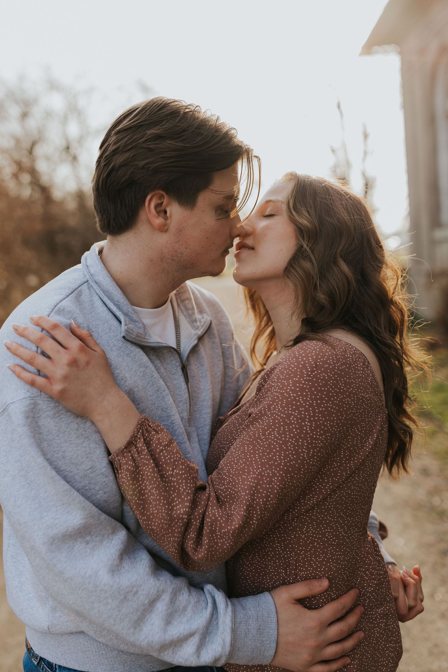 Couple shares a tender kiss outdoors during a romantic golden hour engagement photo session.
