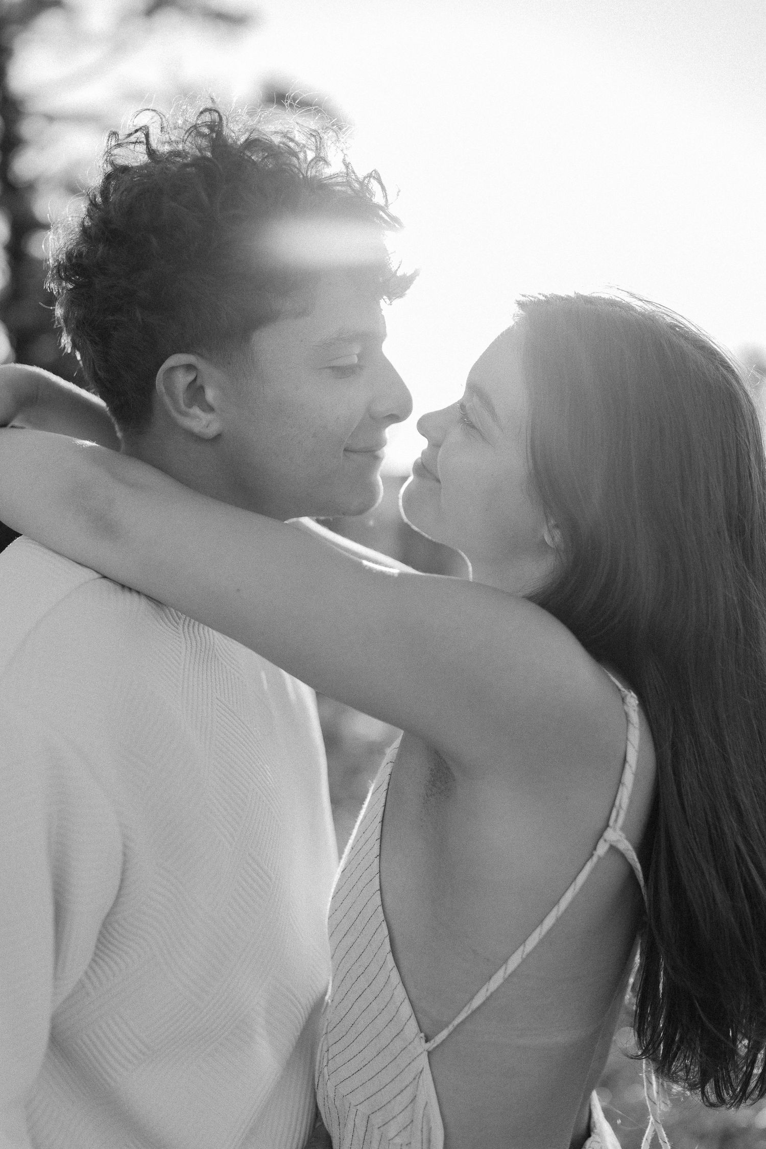 Black and white photo of a loving couple embracing and almost kissing in bright sunlight.