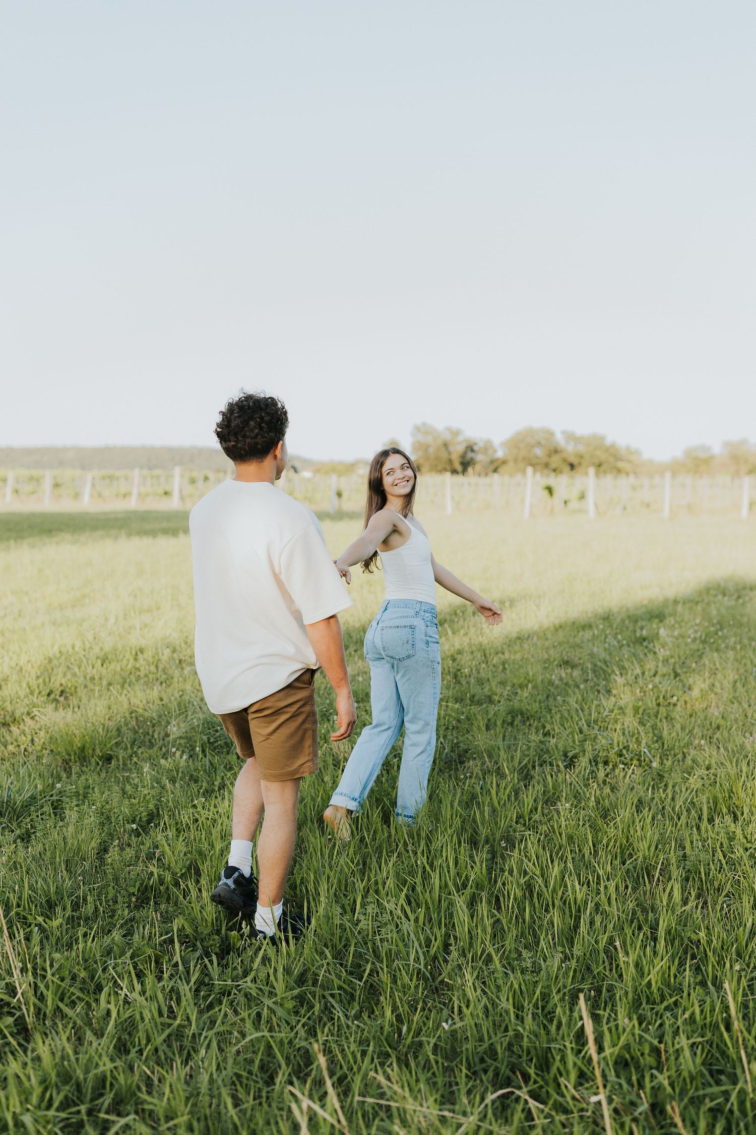 Young couple holding hands in a lush green field during golden hour.