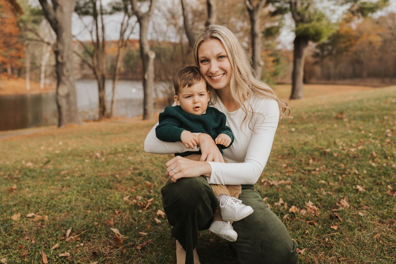 Blonde mother sitting outdoors holding her baby boy during a fall family photo session.