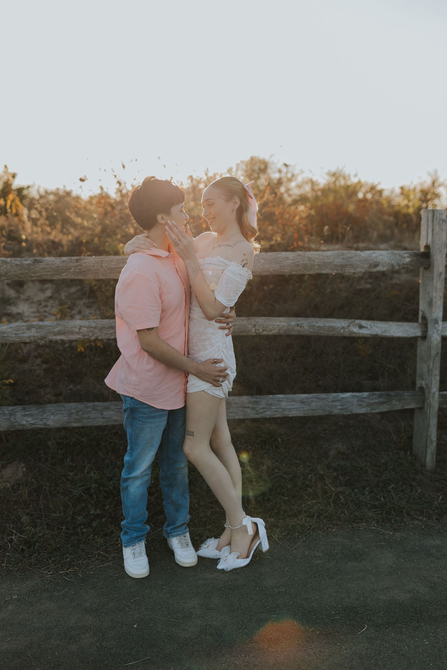 Couple embracing and almost kissing near a rustic wooden fence during a golden hour photo session.