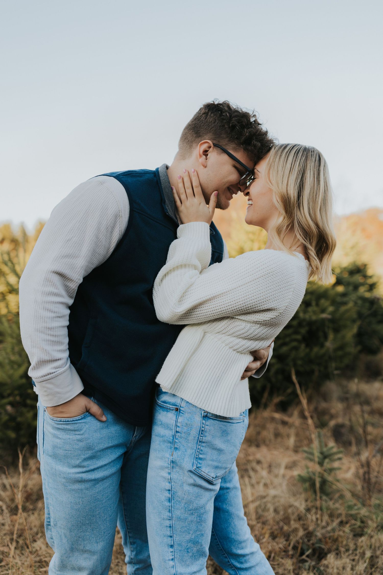 Couple nearly kissing in a golden field at sunset during a fall outdoor engagement photo session.
