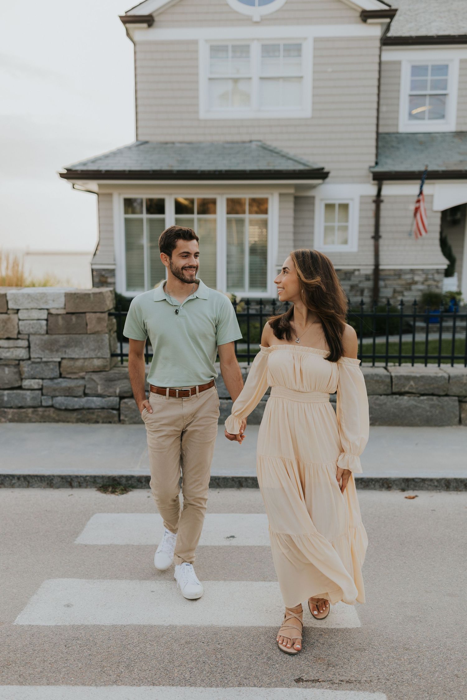 Happy couple holding hands while crossing a street, man in sage polo and khakis, woman in cream maxi dress.