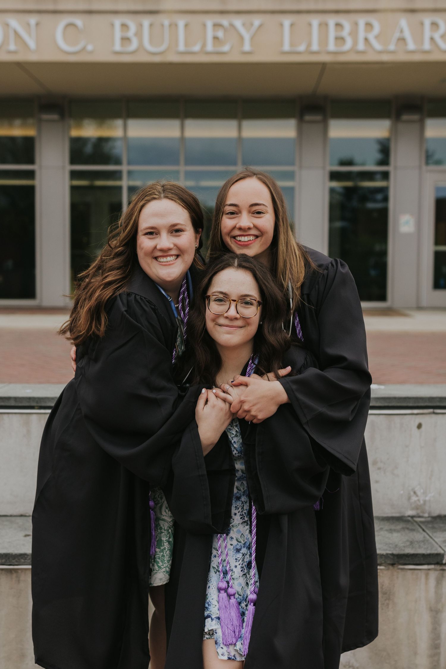 Three smiling nursing graduates hugging in front of Buley Library.