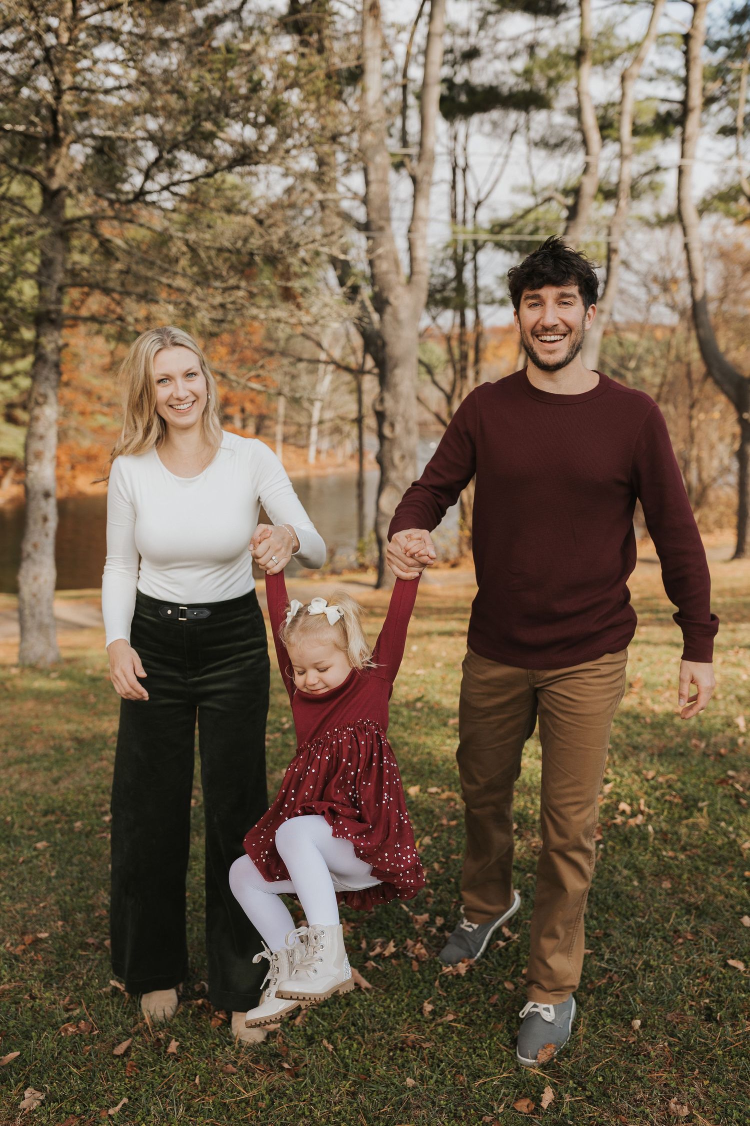 Happy family of three swinging their toddler daughter between them in an autumn park.