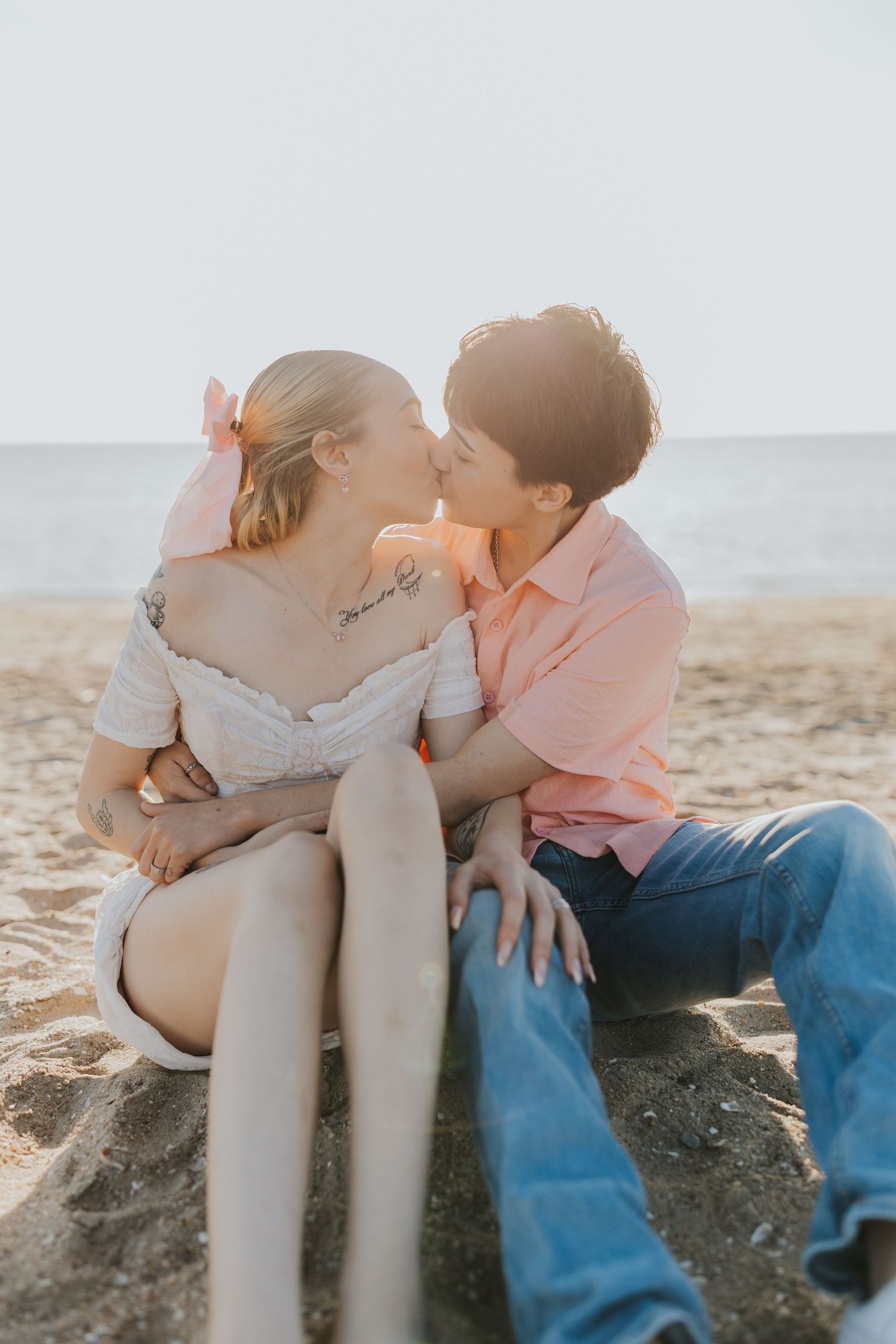 Couple sharing a romantic kiss while sitting together on a sandy beach at golden hour.