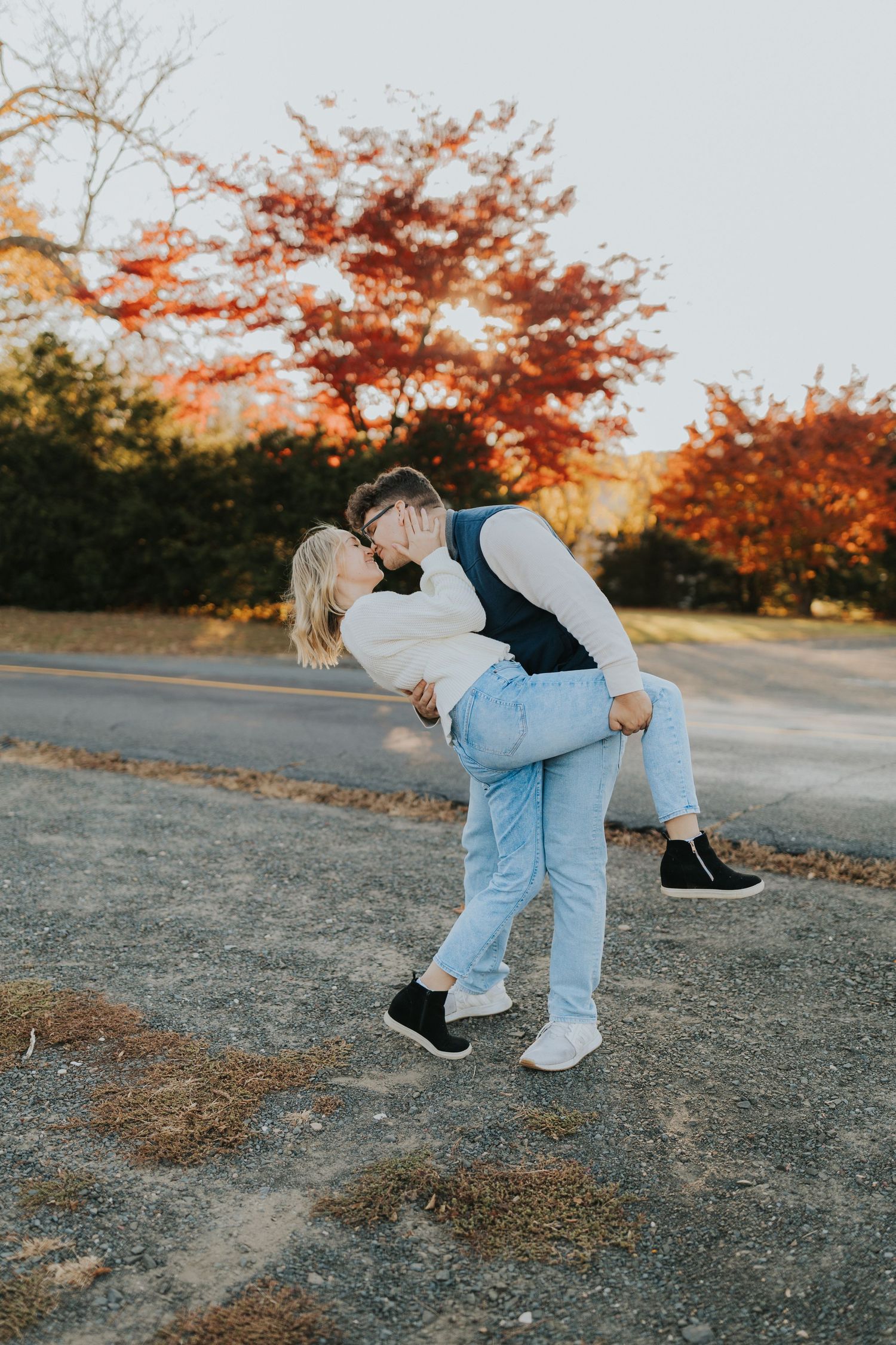 Man dips woman for a romantic kiss outdoors with vibrant red autumn foliage in the background.