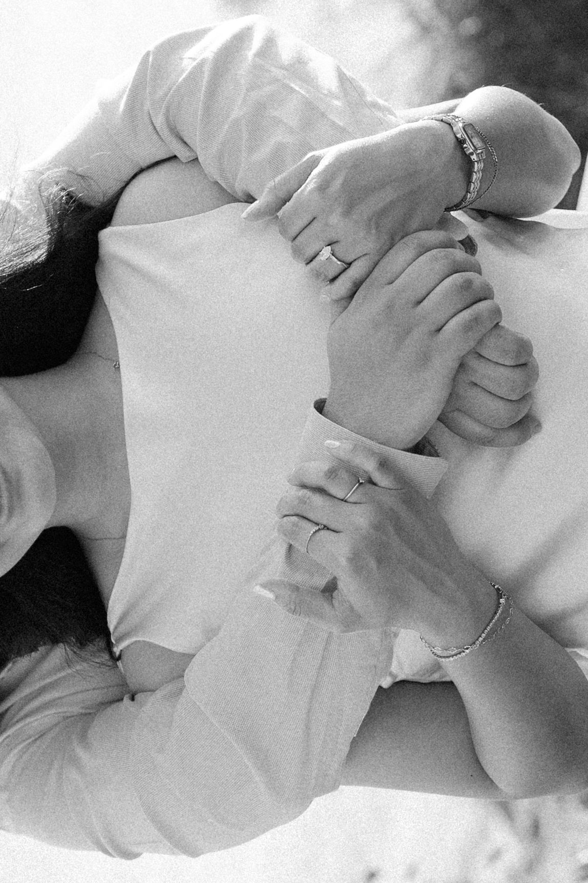 Black and white photo of a couple holding hands, wearing rings and bracelets, embracing tenderly.