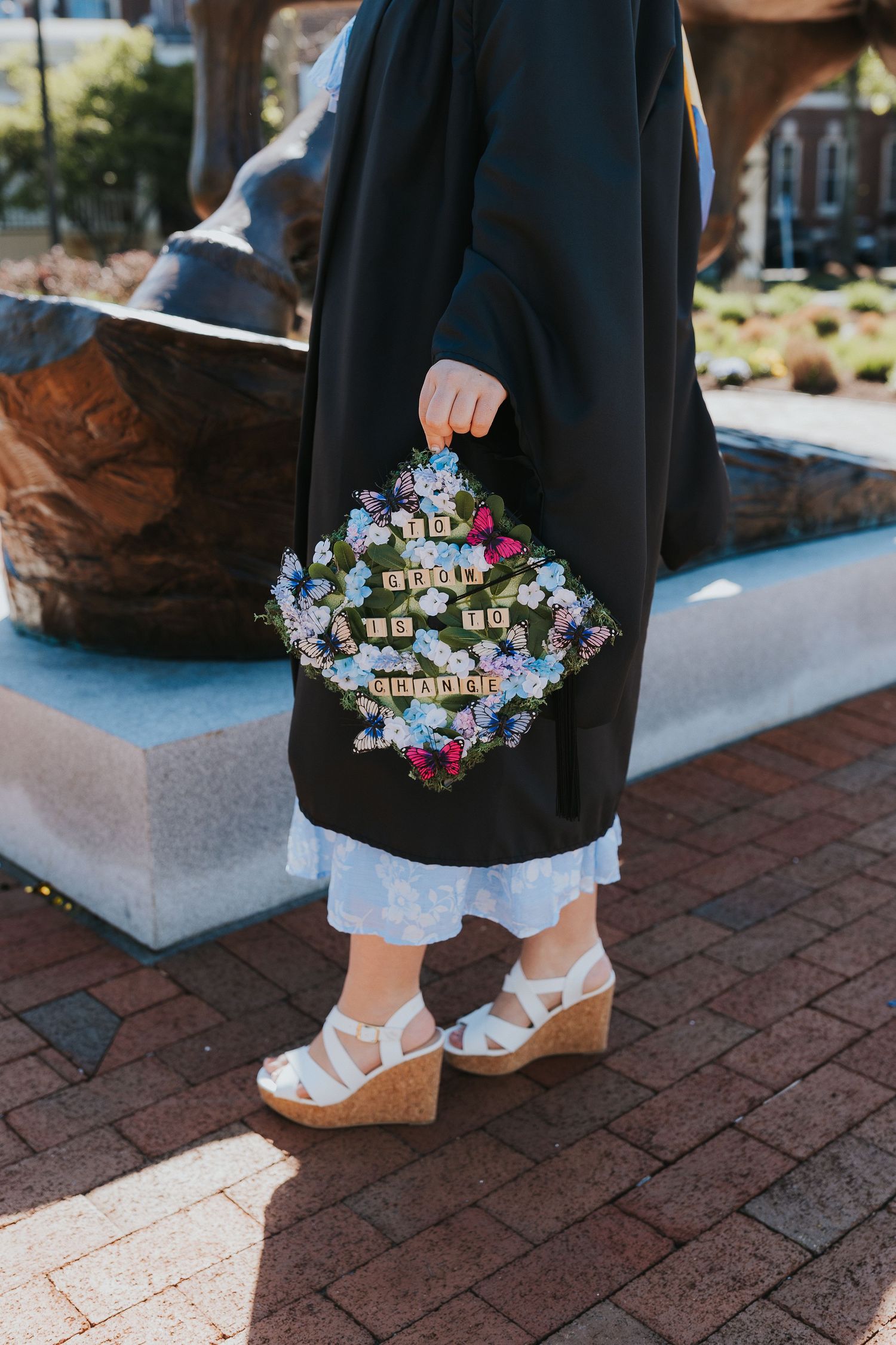Close-up of decorated graduation cap with floral design and Scrabble tiles held by robed graduate.