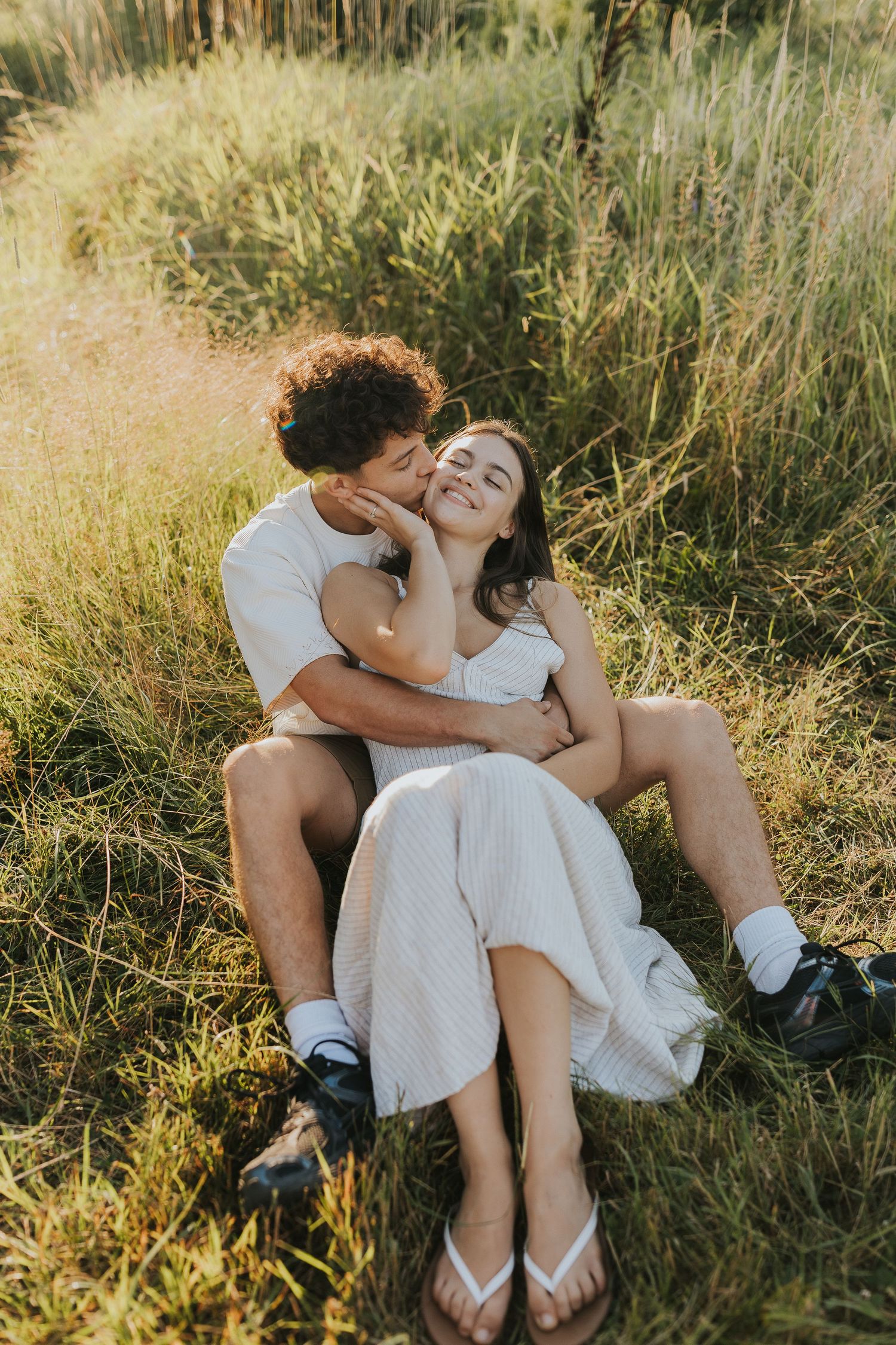 Couple sitting together in tall grass field sharing a romantic moment in golden sunlight.