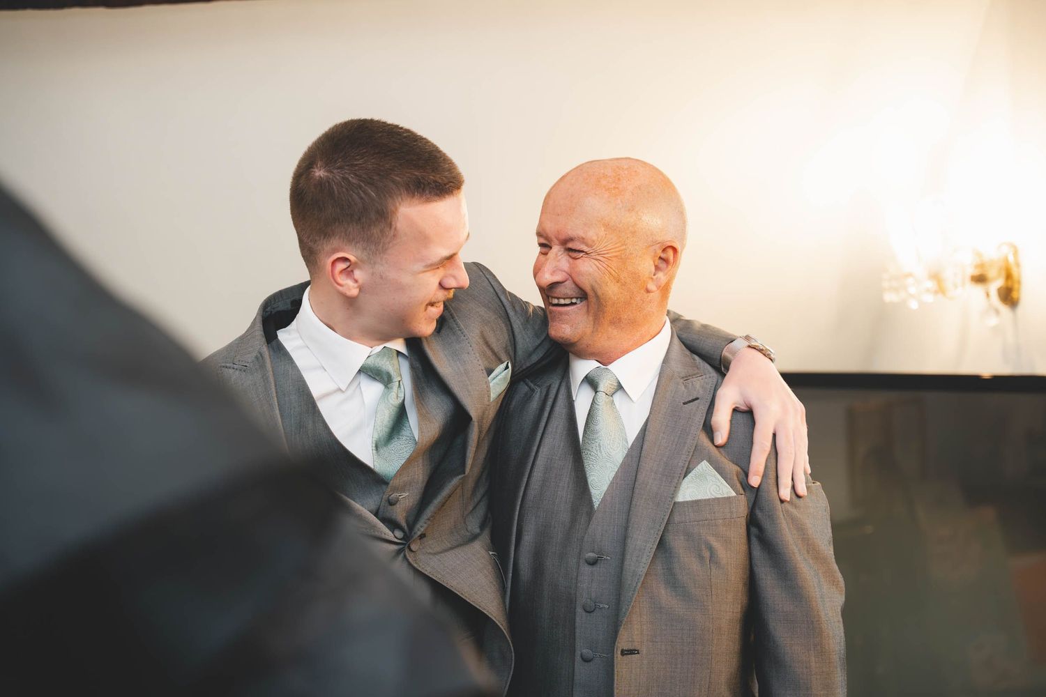 2 men smile at each other and share an embrace at a wedding in telford