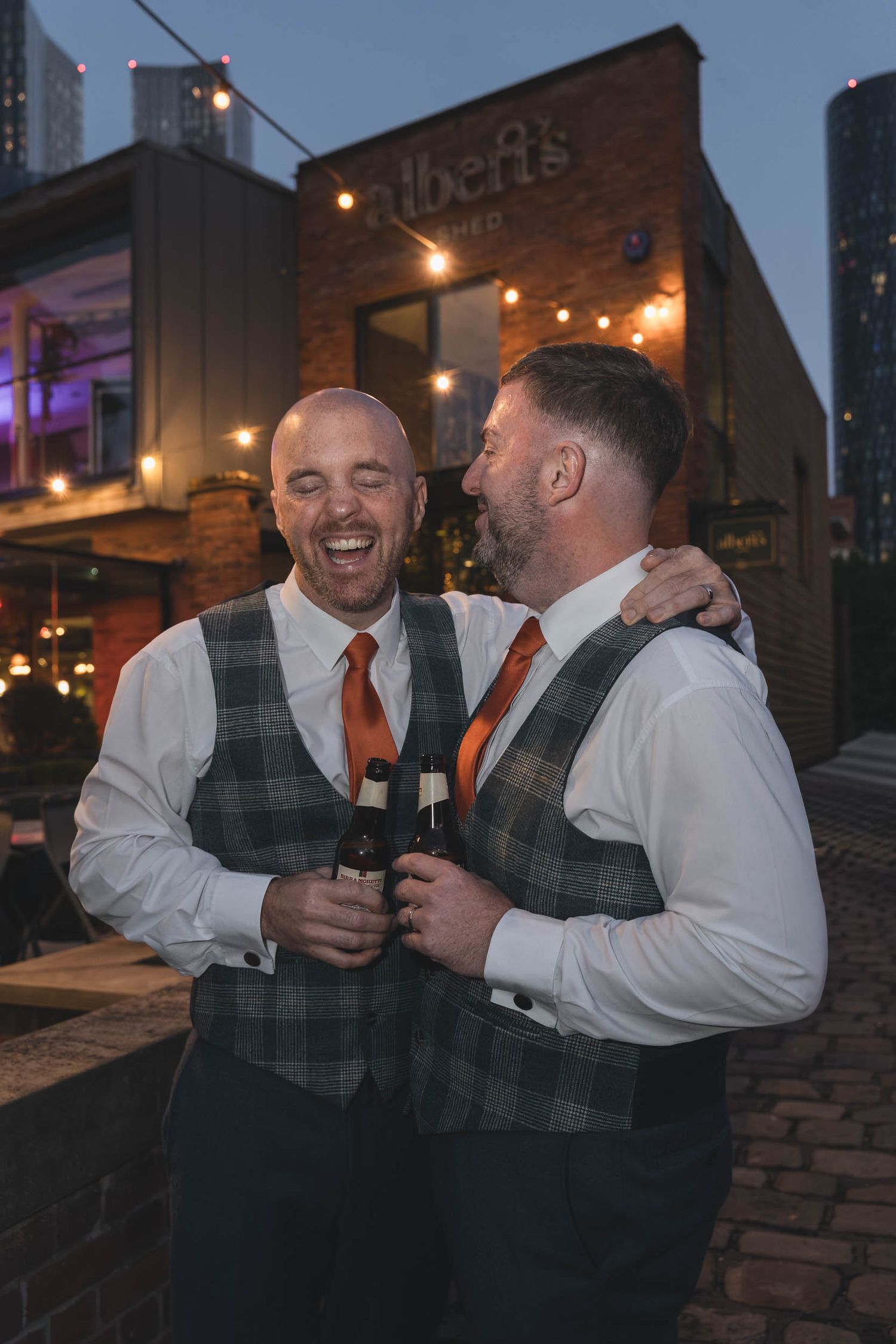2 grooms smile and laugh naturally at Castlefield Rooms wedding venue in Manchester