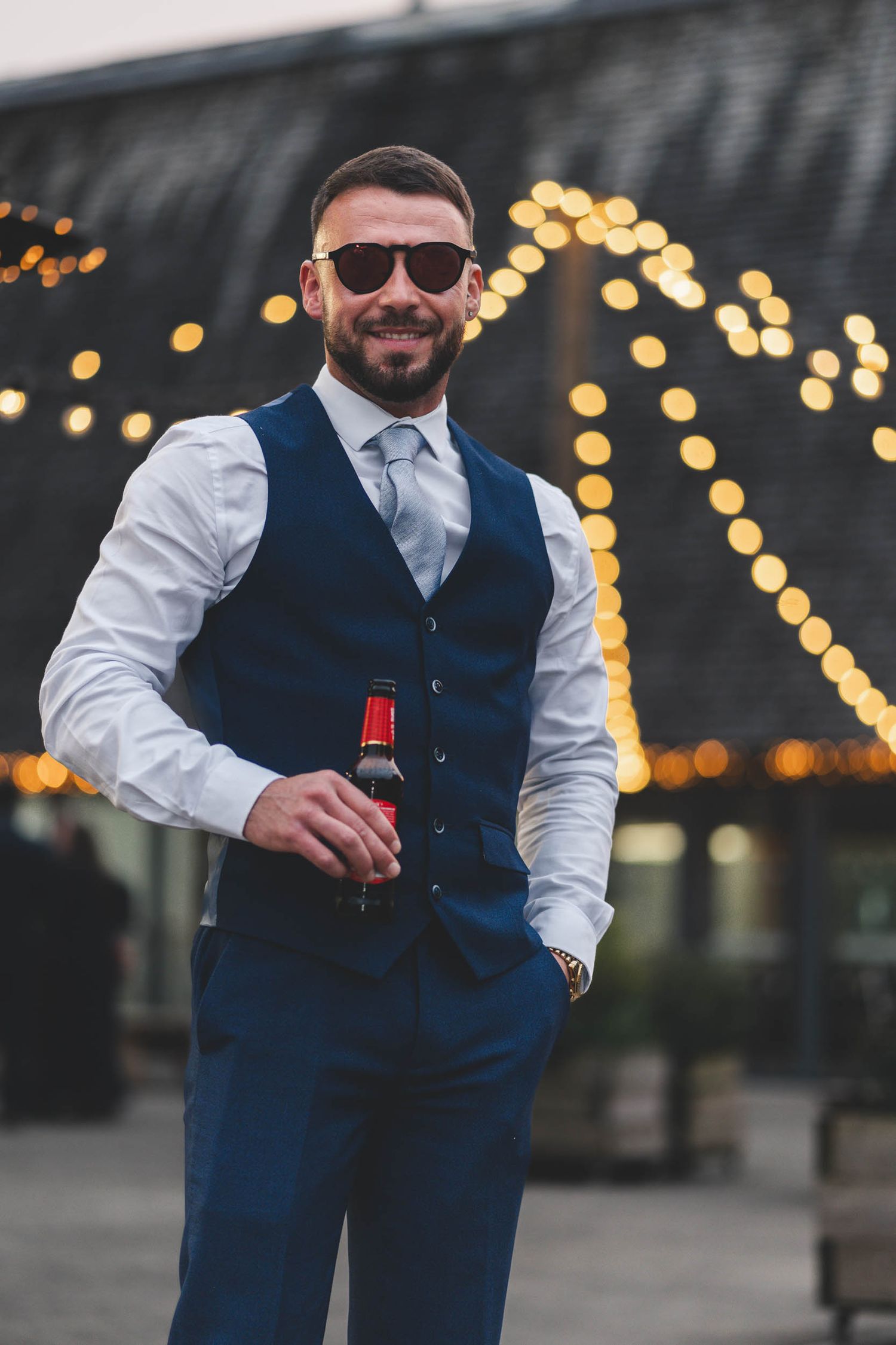 the best man at a wedding smiles in front of lanterns near Preston