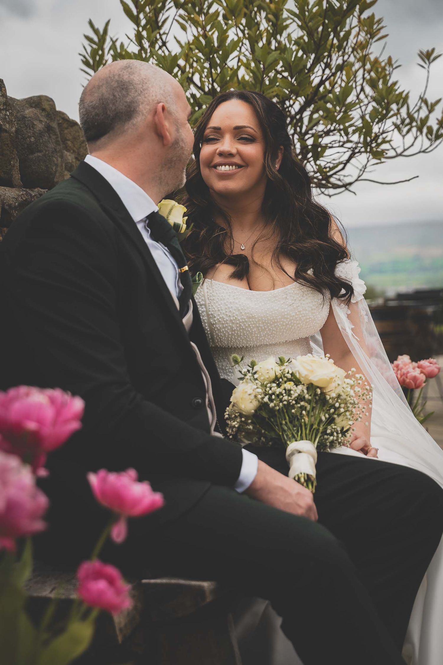 a bride and groom smile candidly among flowers in lancashire