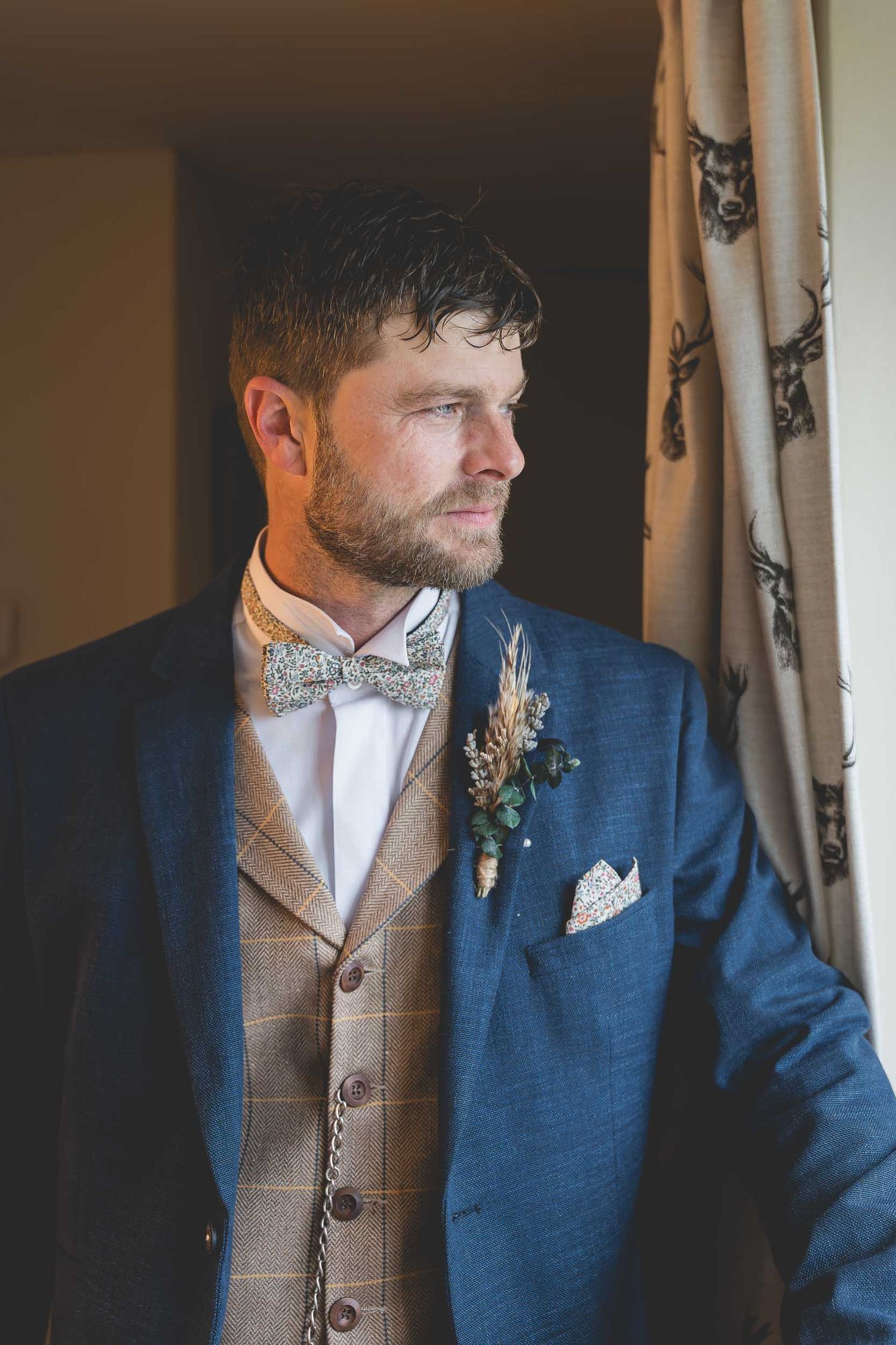 a groom in a blue suit looks out of a window in County Durham