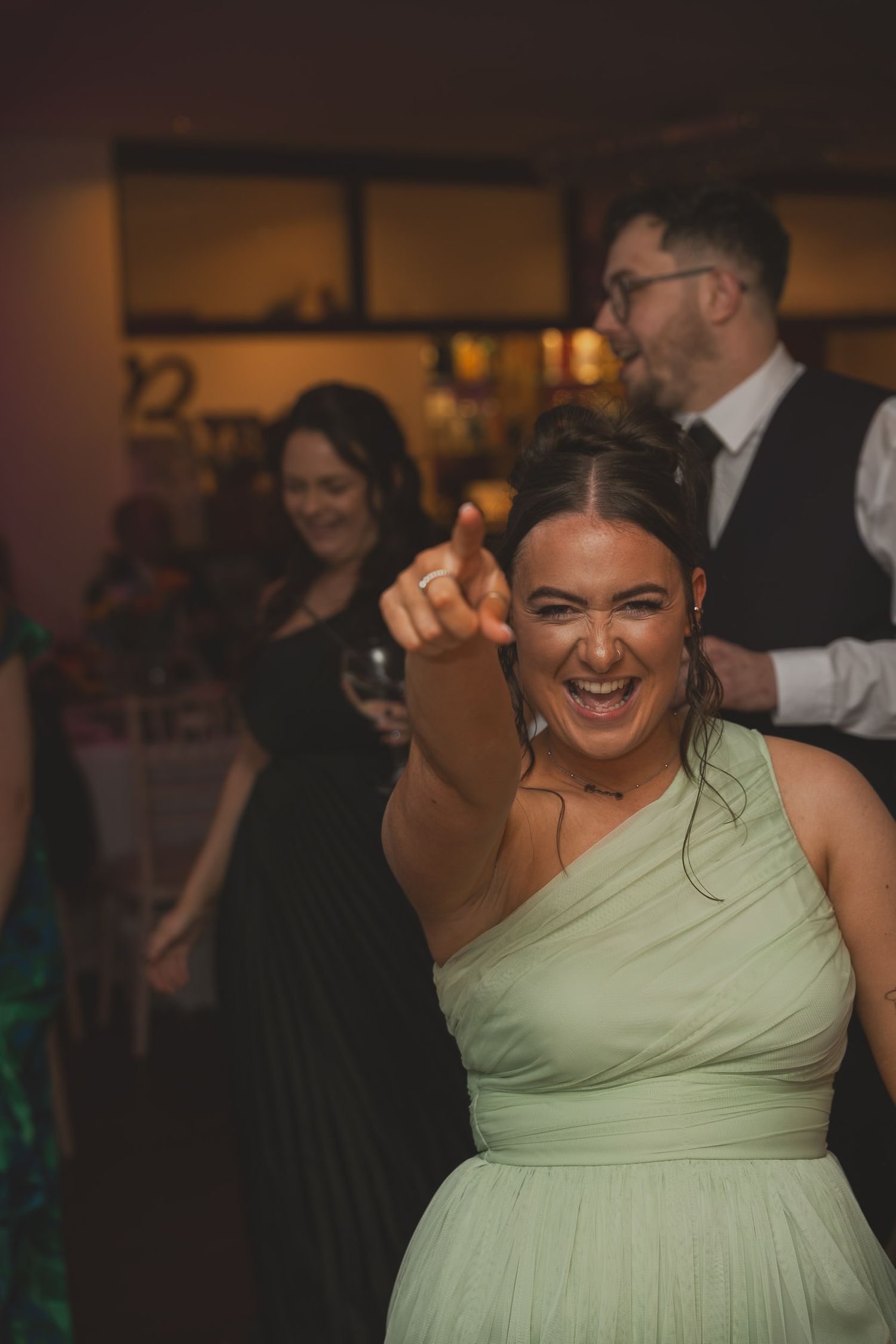 a bridesmaid smiles and points at a camera during a wedding reception in Greater Manchester