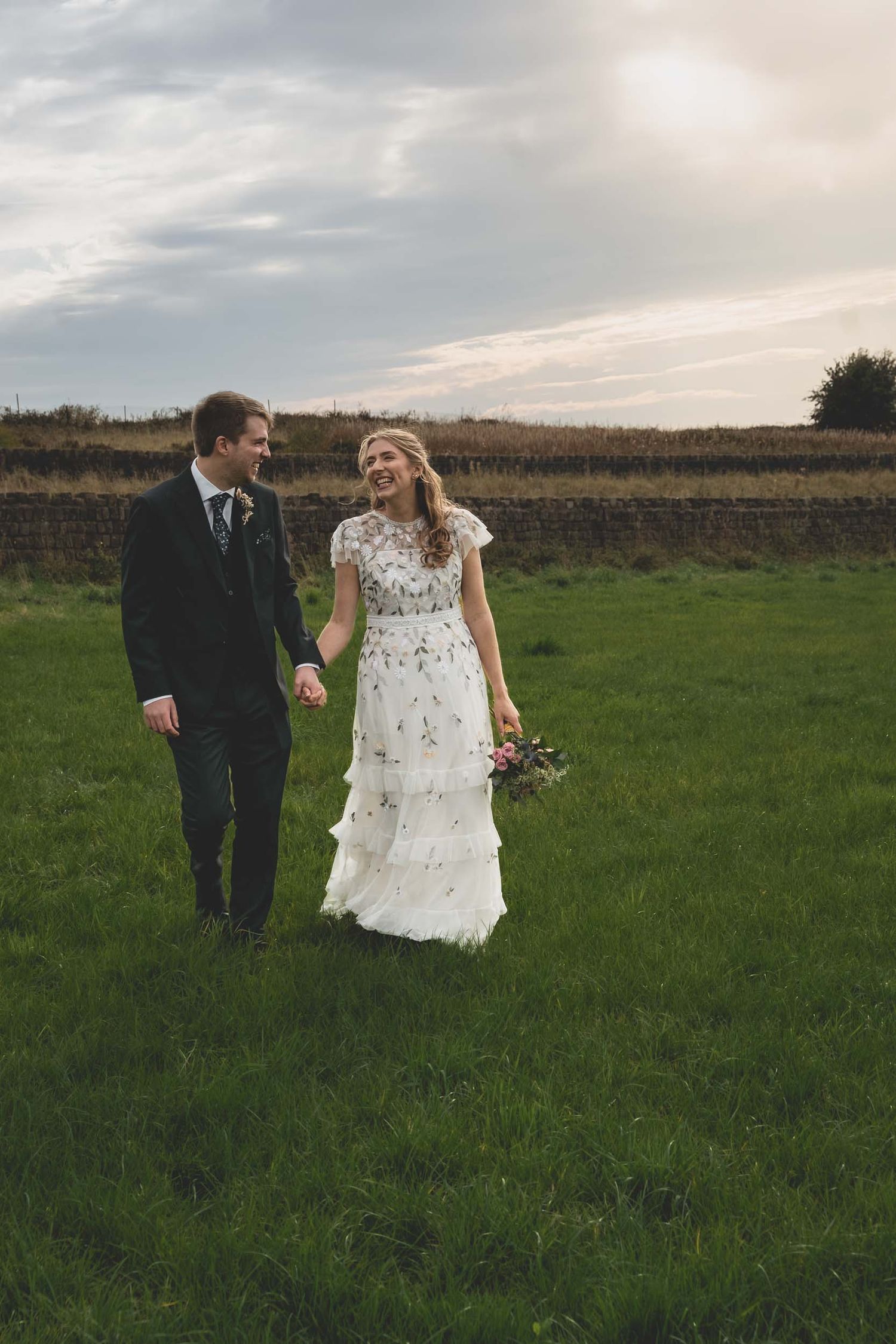a bride and groom smile as walking through the fields in Parbold