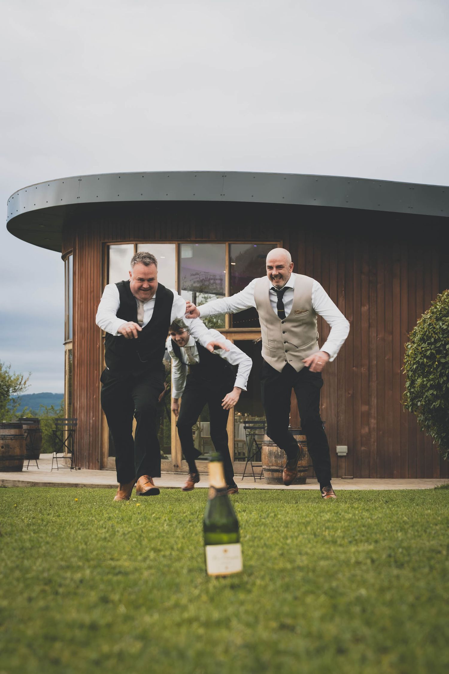 a groom and his best men running towards a bottle of prosecco at The Out Barn wedding venue in Ribble Valley
