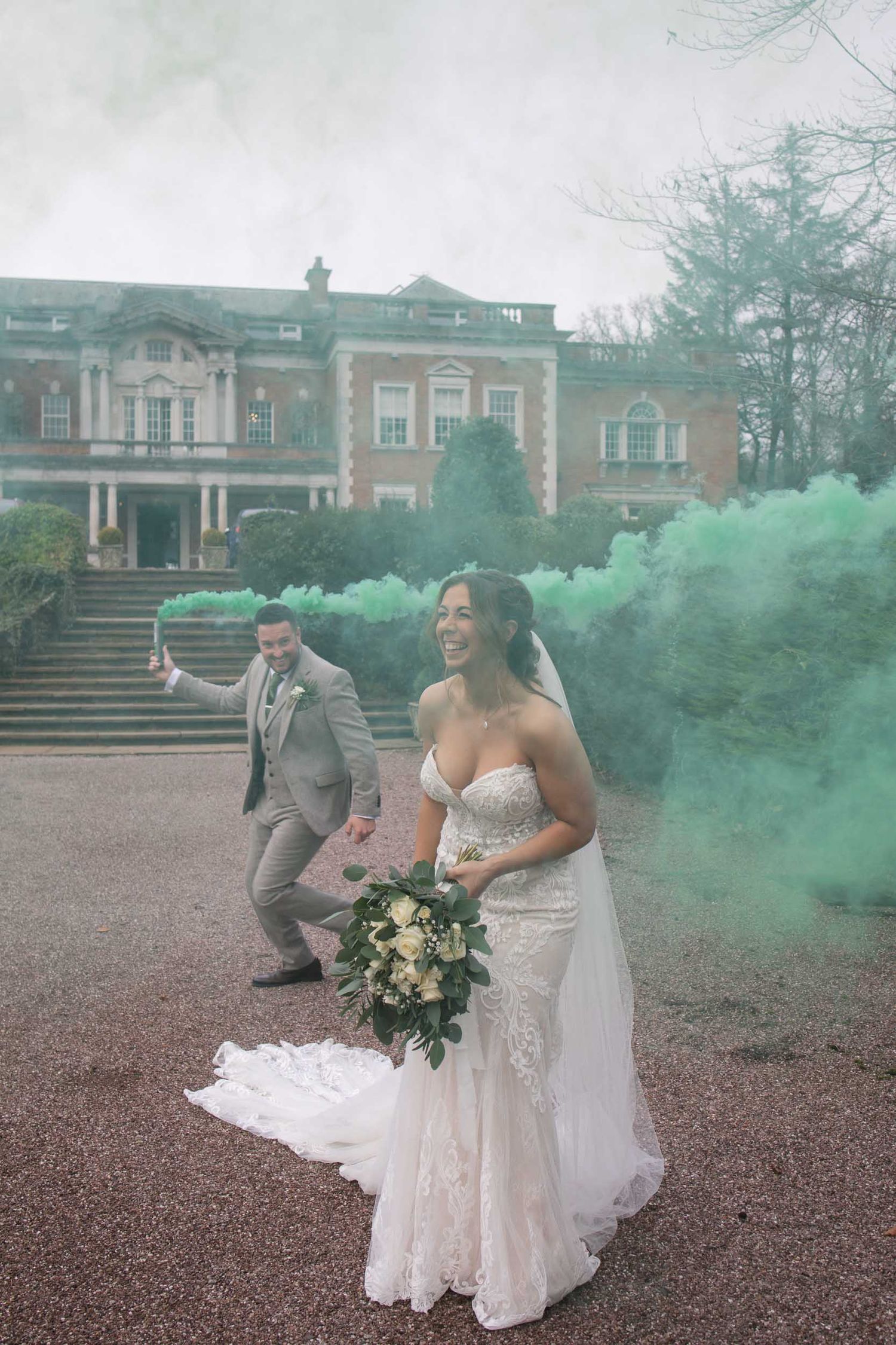 a bride and groom playing with green smoke bombs at Mitton hall wedding venue in clitheroe