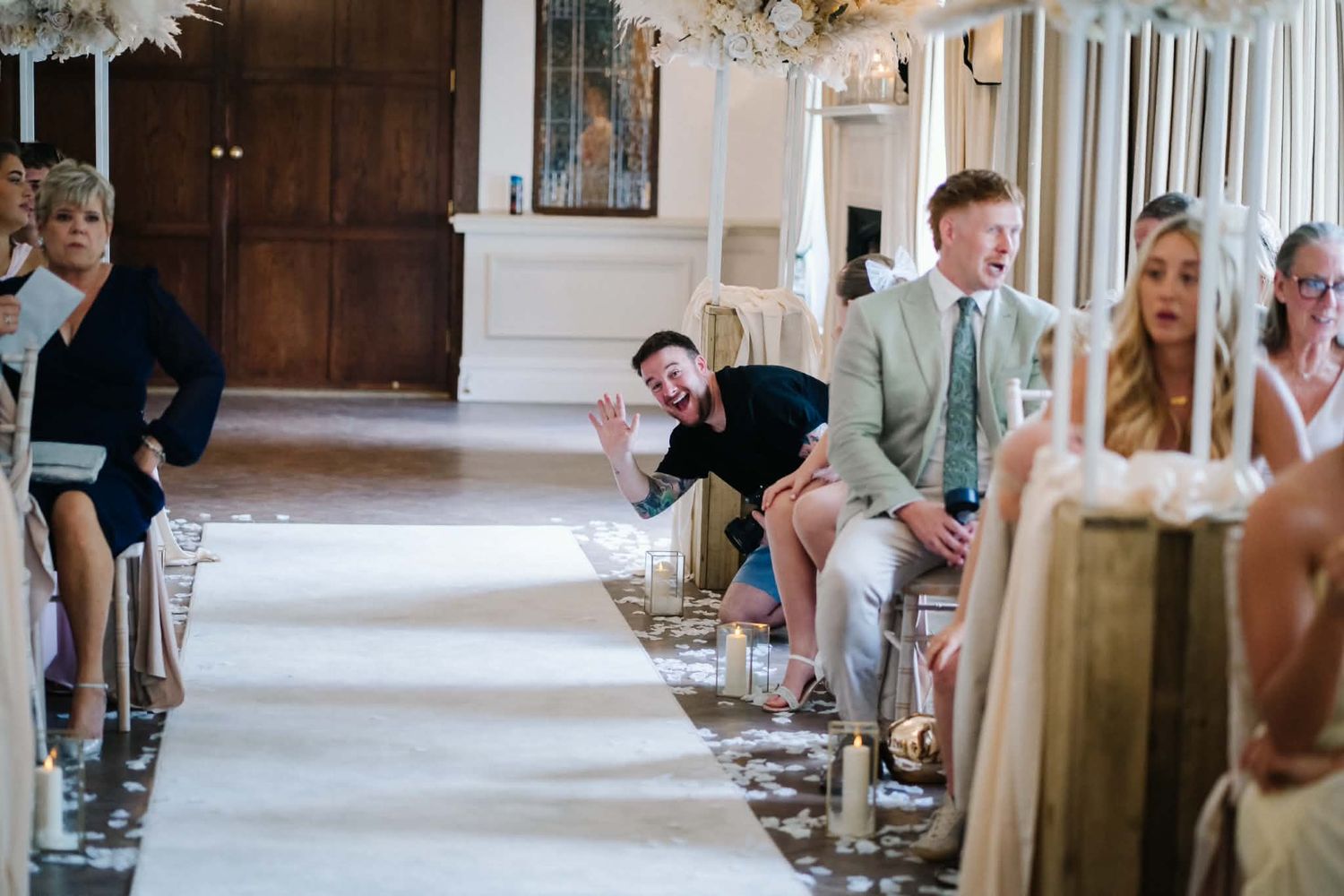 a wedding photographer smiling and waving from the aisle of a wedding ceremony at battle Hall near Preston