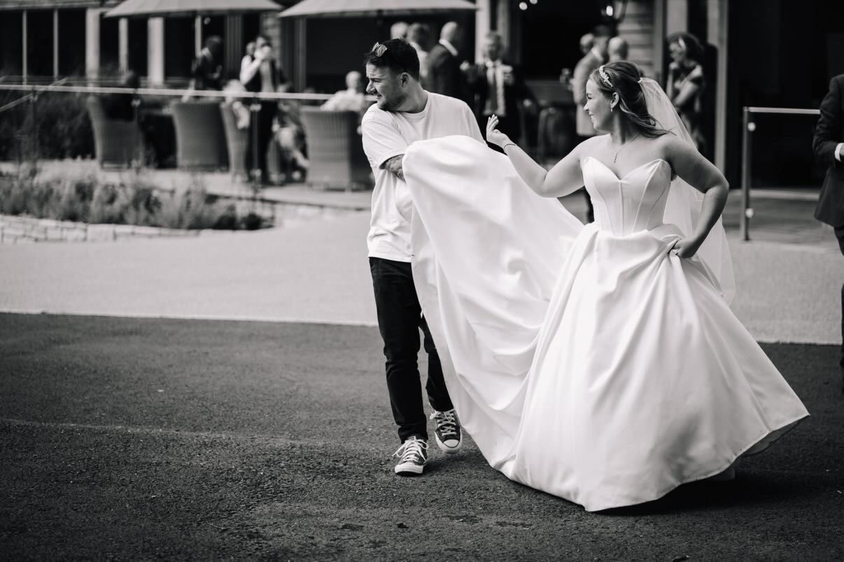 A black and white shot of a wedding photographer helping a bride with her dress on her wedding day at Hobbit Hill wedding venue in clitheroe