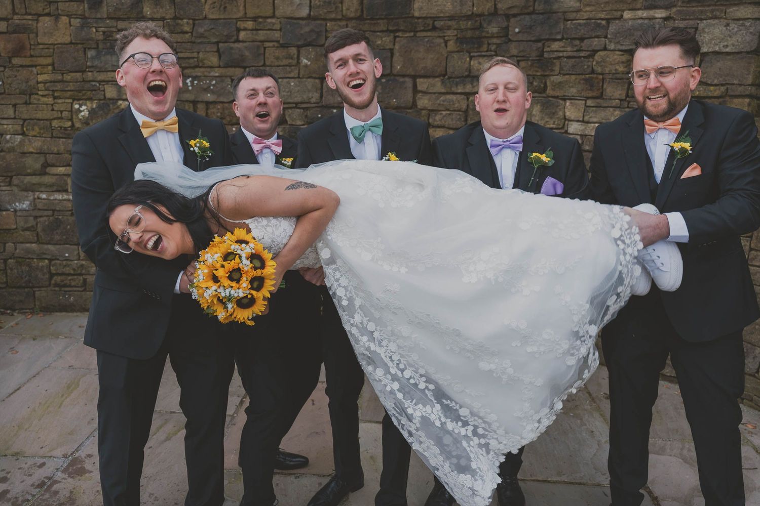 groomsmen holding up a bride as they all laugh at a wedding in greater manchester