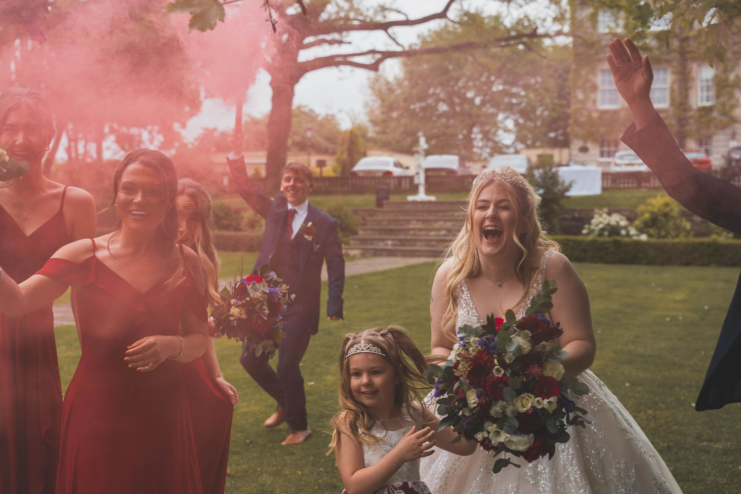 a bride laughs as a groomsman sets off a red coloured smoke bomb in Sheffield