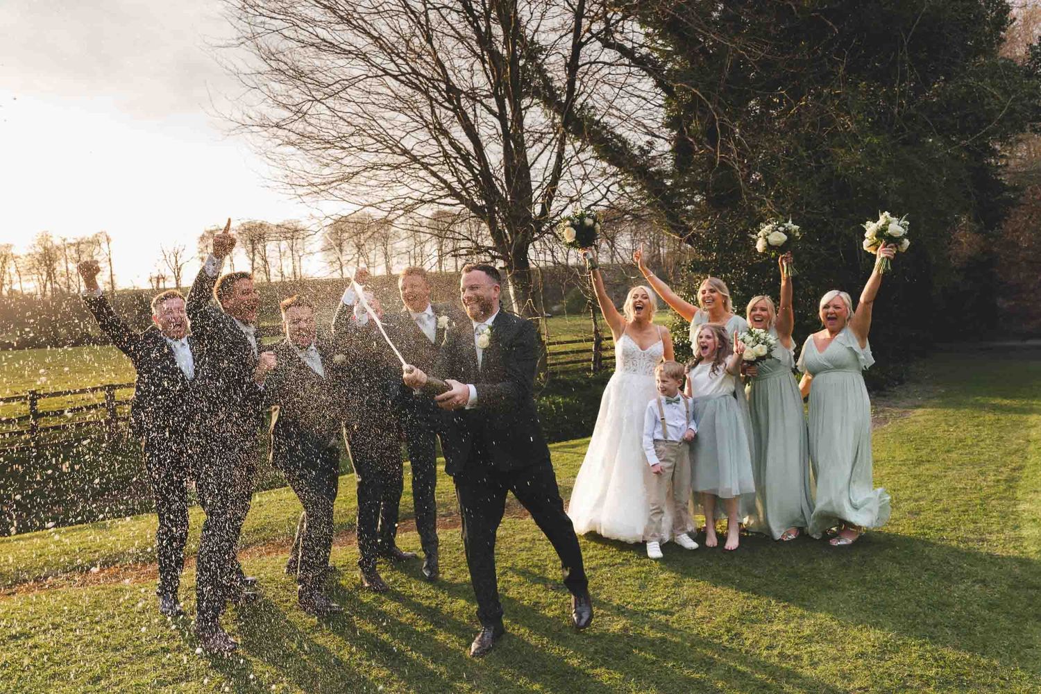 a groom sprays champagne as the wedding party cheer in the sun at a wedding in lancashire