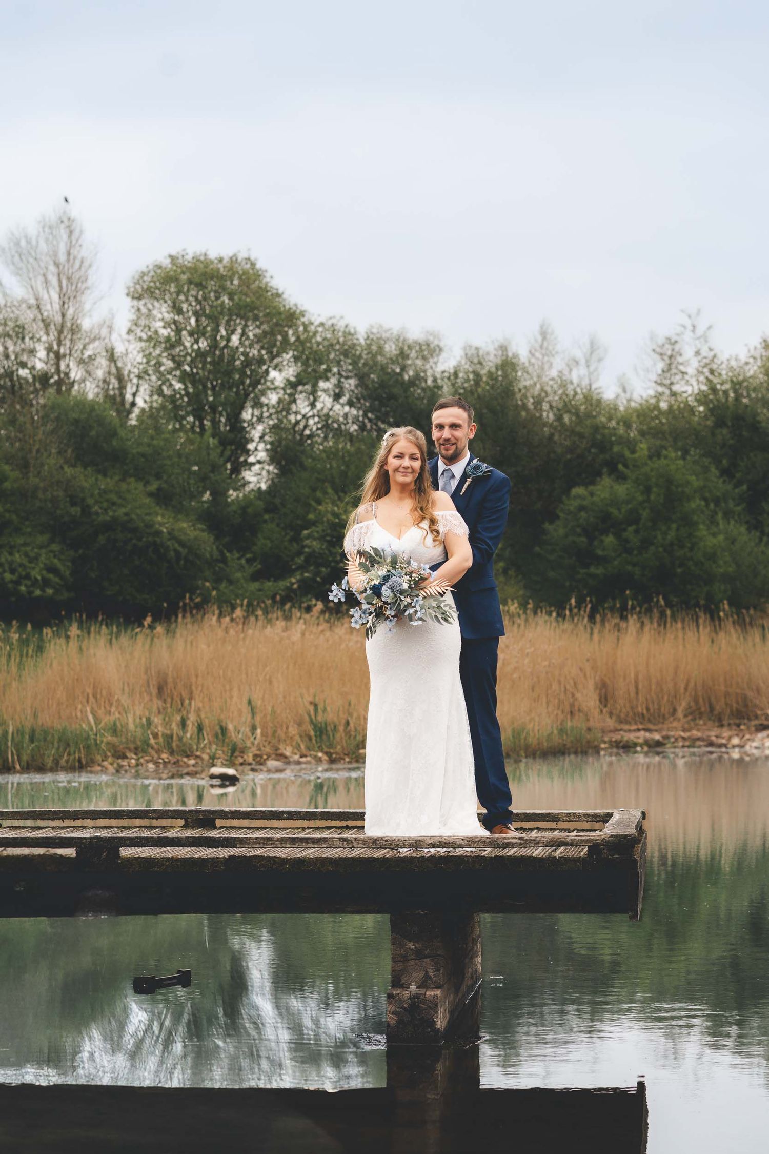 a bride and groom pose and smile overlooking the water at Brockholes near Preston