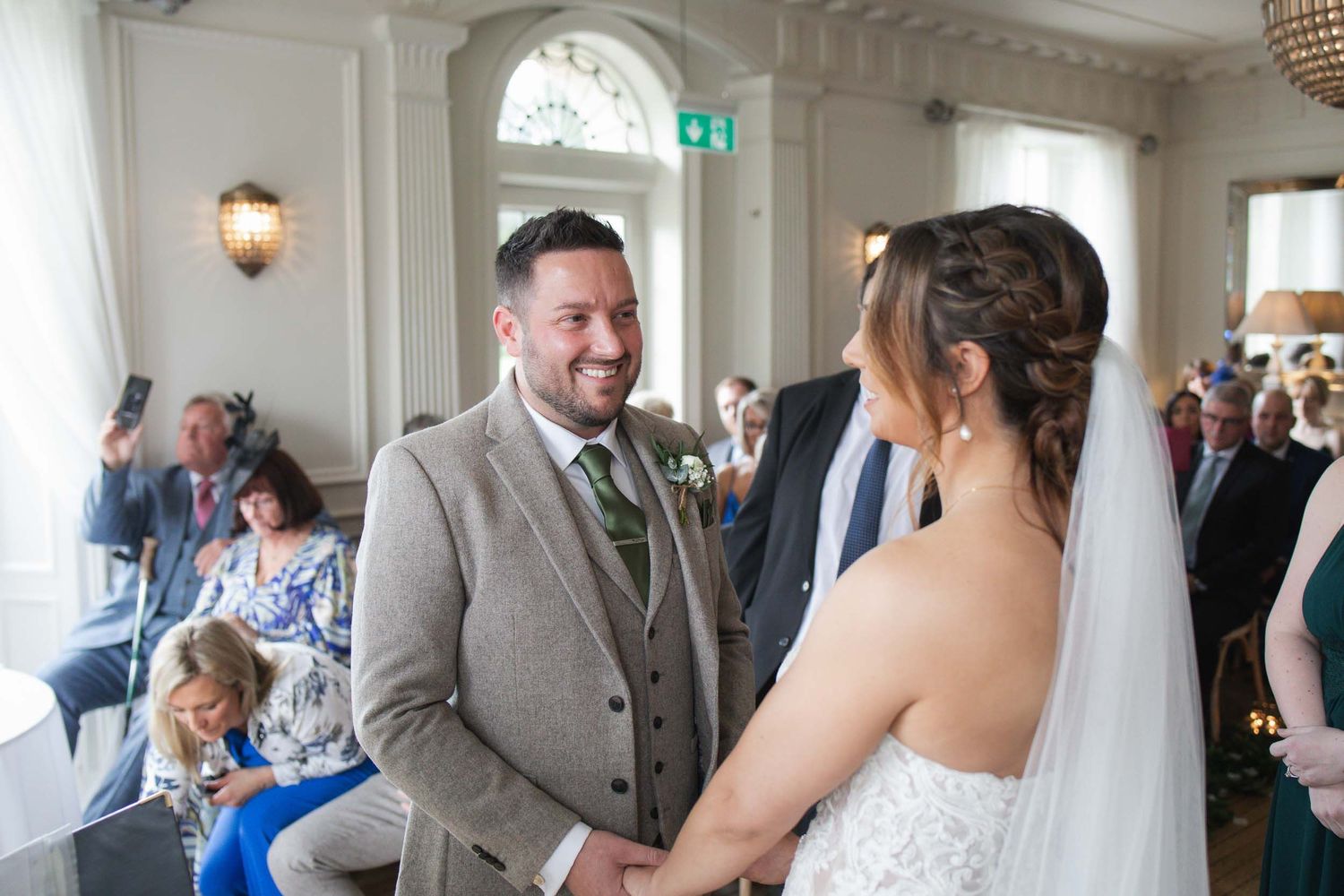 a groom smiles at the bride during a ceremony at Mitton Hall