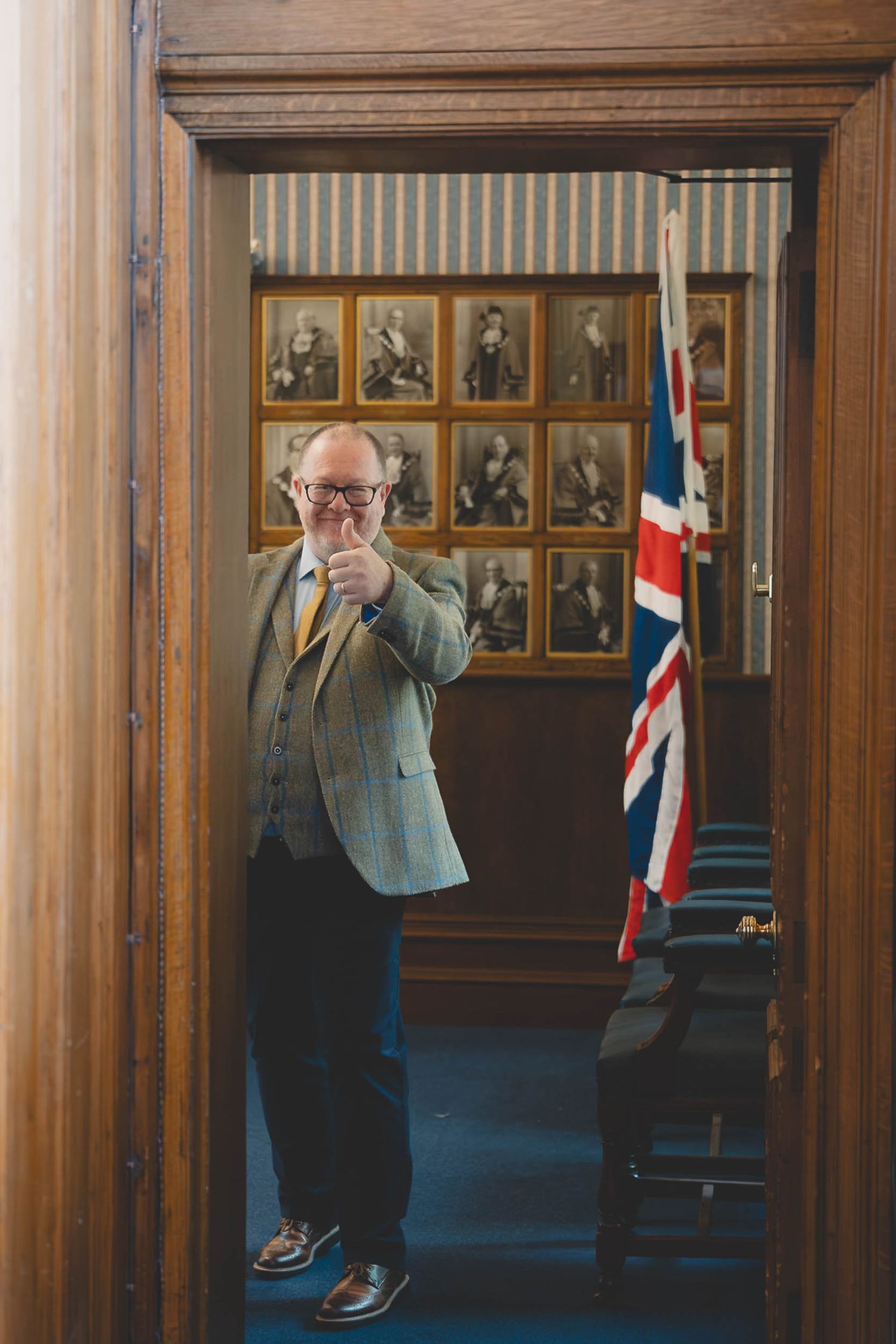the father of the bride giving a thumbs up from a back room in Southport town hall during a wedding ceremony