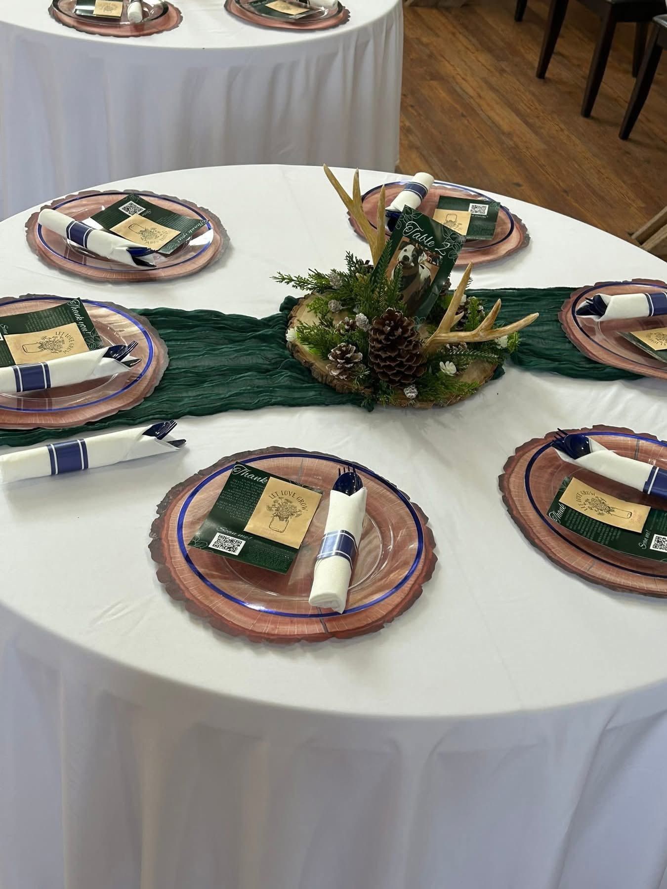 Elegant round wedding table with green runner, antler centerpiece, pine cones, and wood charger plates.