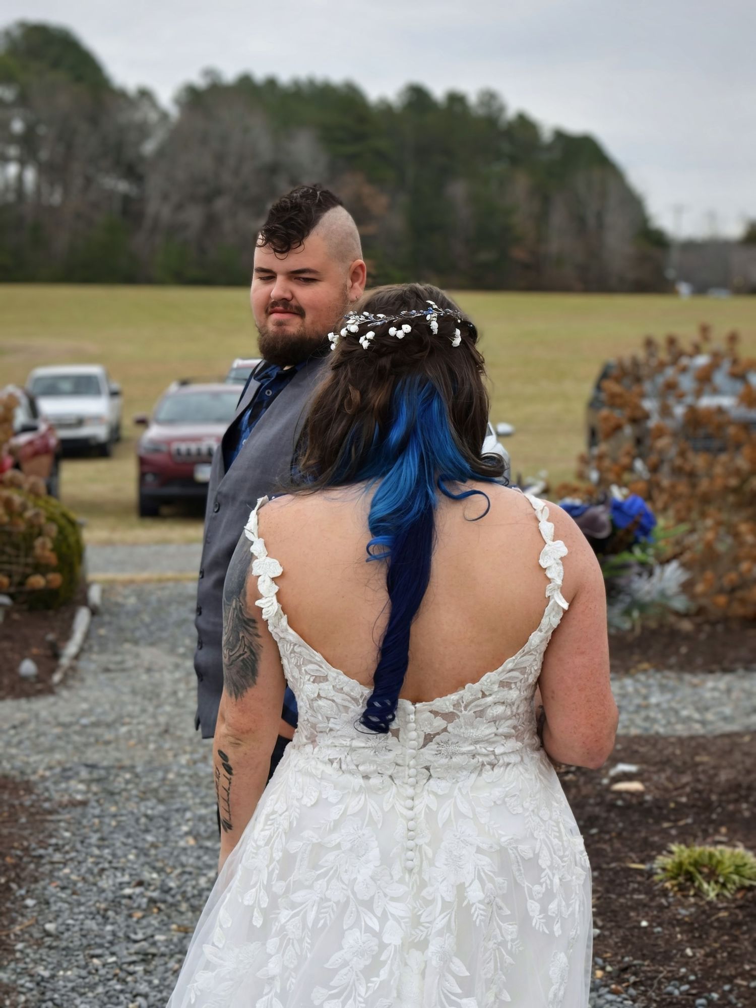 Groom gazing at bride during first look outdoor wedding moment, bride in backless lace gown.