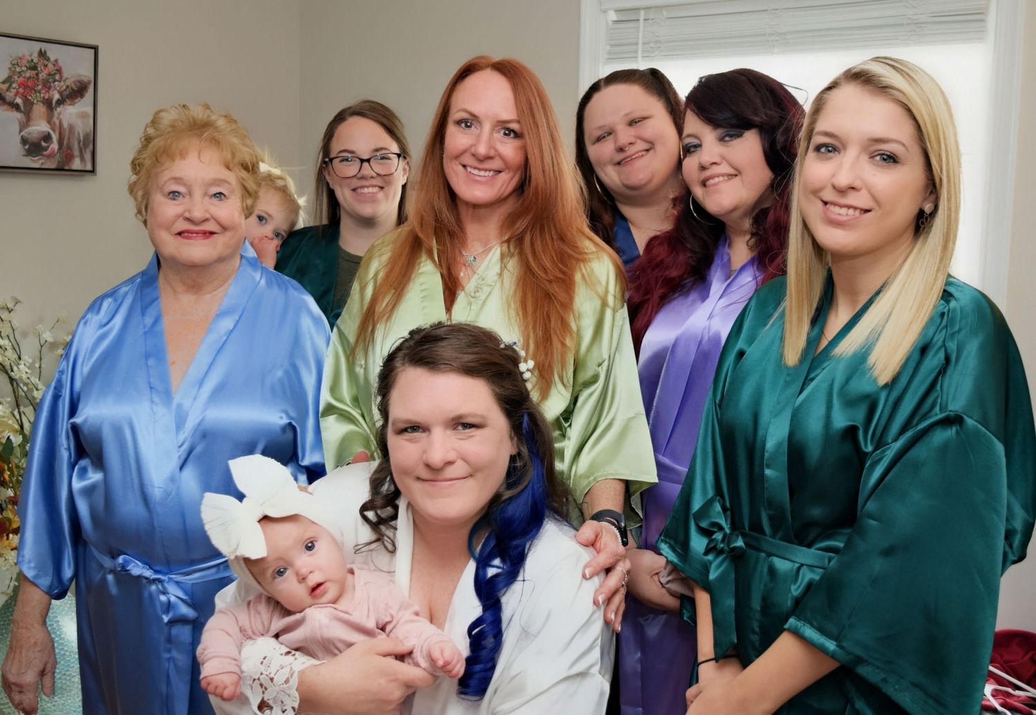 Bridal party in colorful satin robes posing together indoors before wedding ceremony.