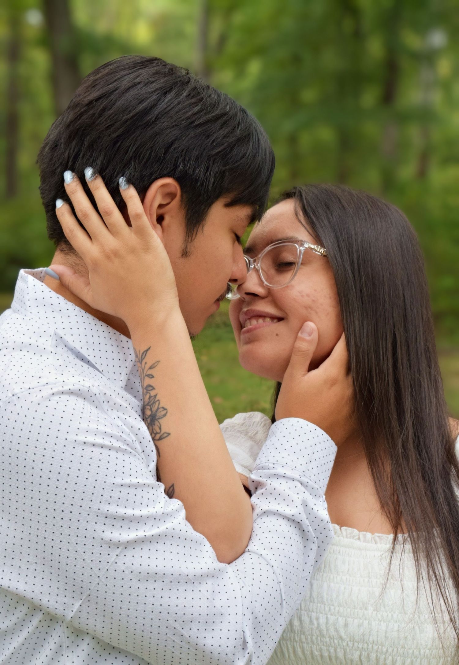 Romantic couple almost kissing outdoors in a green forest during an engagement photo session.