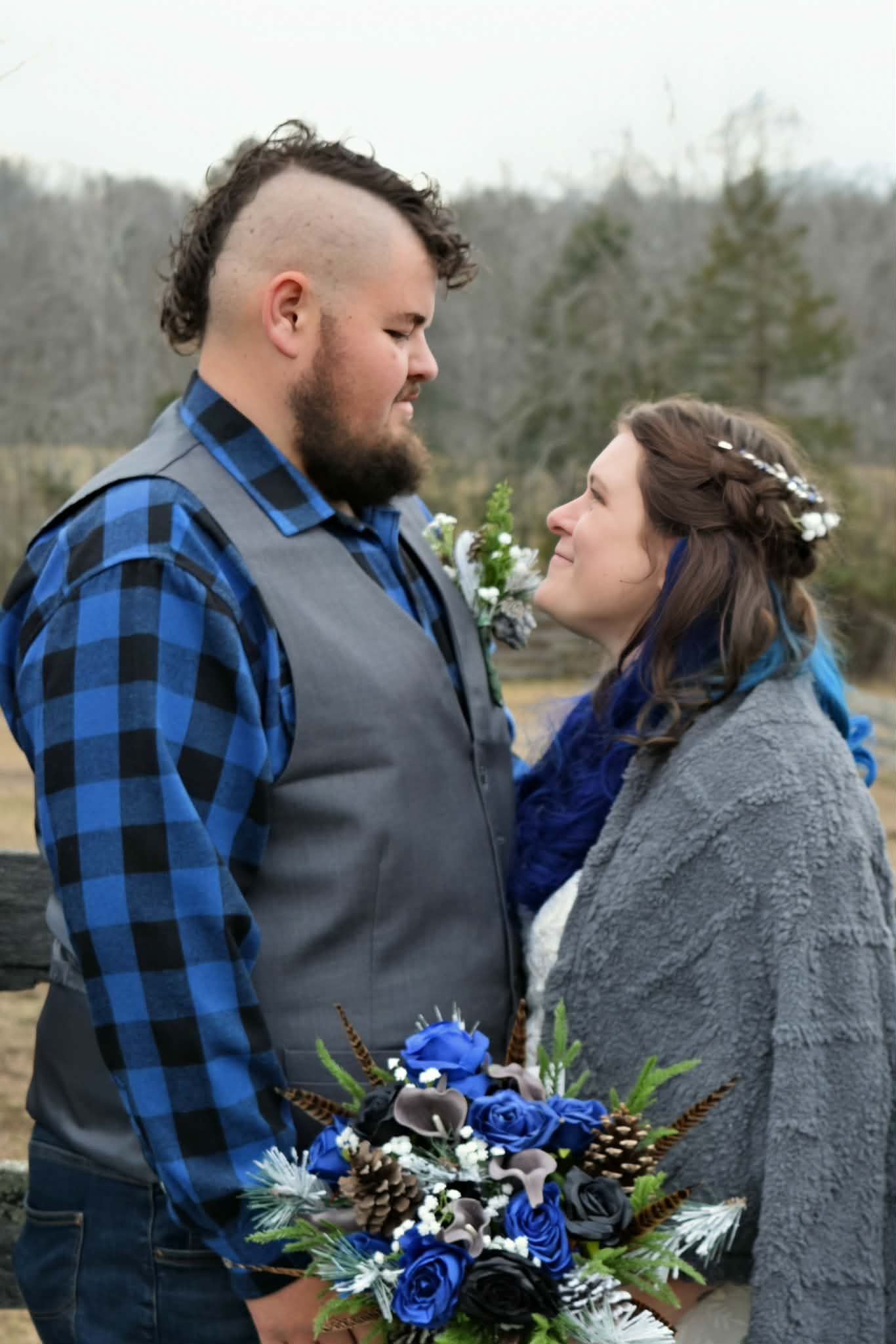 Couple gazing at each other outdoors, bride holding blue floral bouquet in winter.