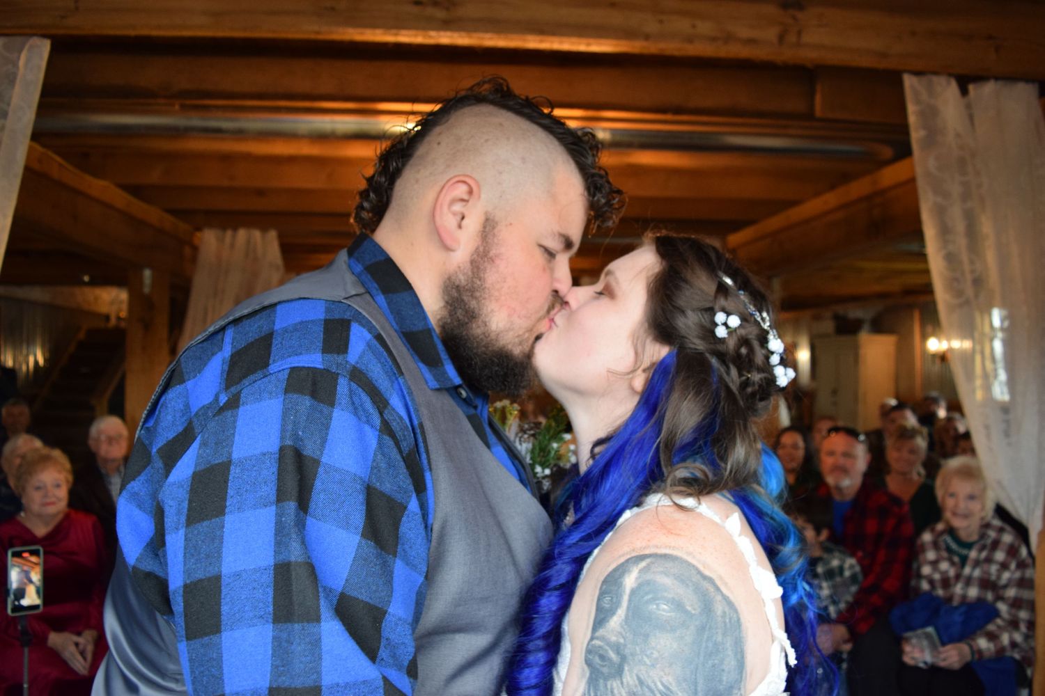 Bride and groom sharing romantic first kiss at rustic indoor wedding ceremony.