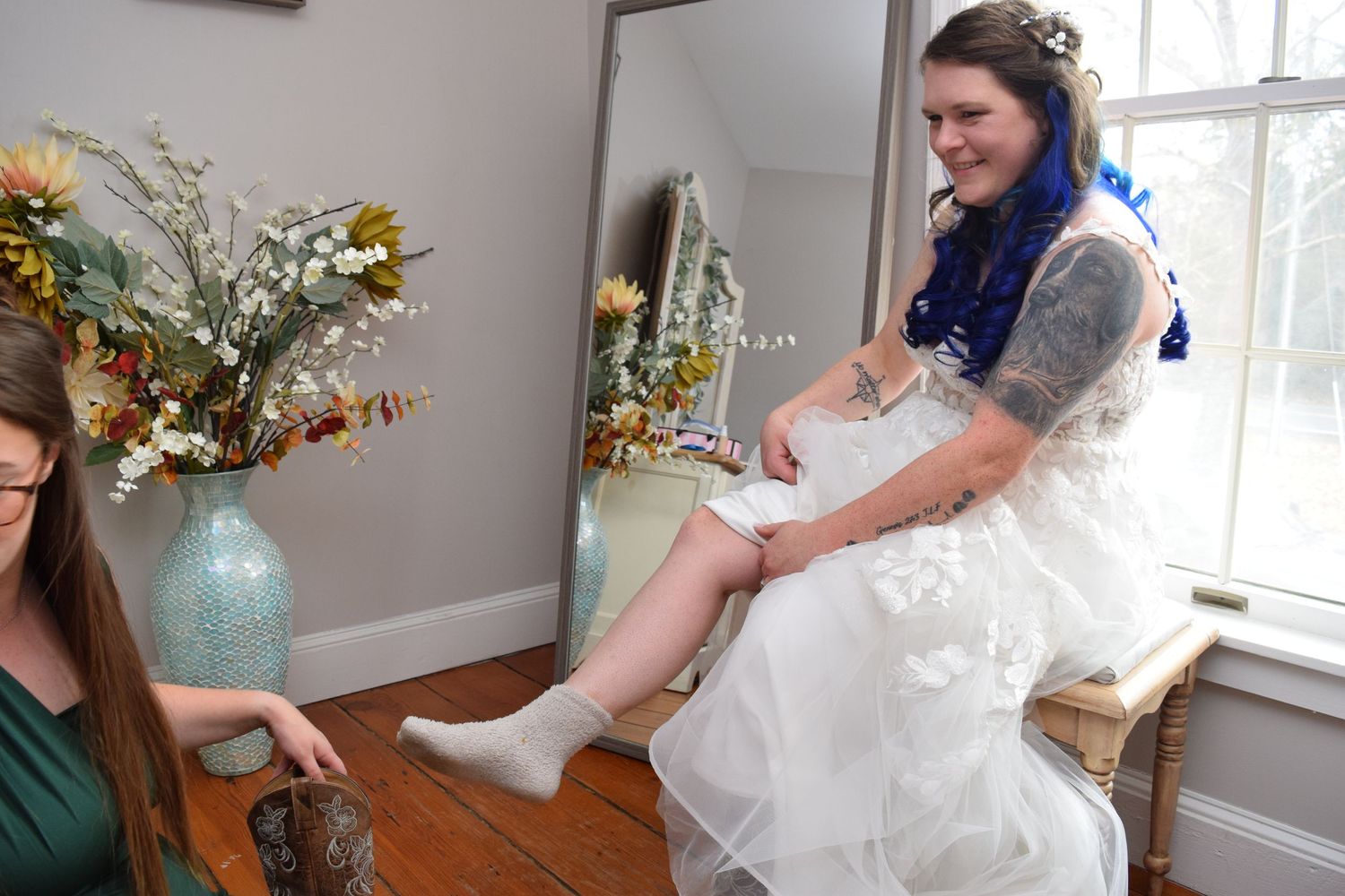 Smiling bride with blue ombre hair putting on white socks before wedding ceremony.