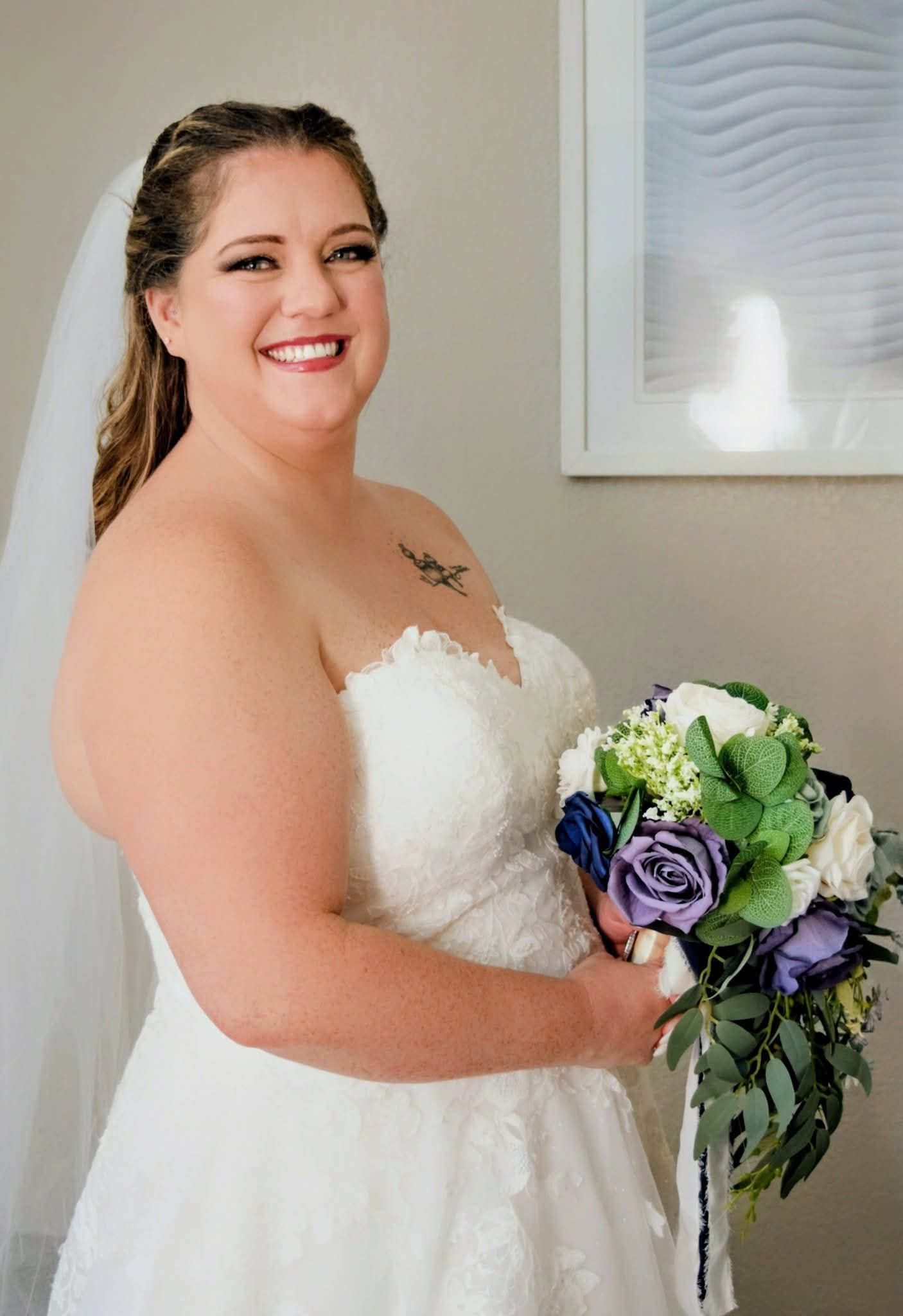 Radiant bride in strapless lace wedding dress holding purple and blue bridal bouquet.