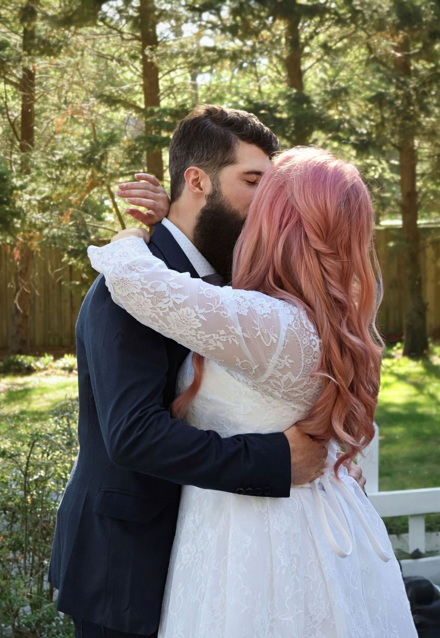 Bearded groom and pink-haired bride share their first kiss as newlyweds during outdoor backyard wedding ceremony.
