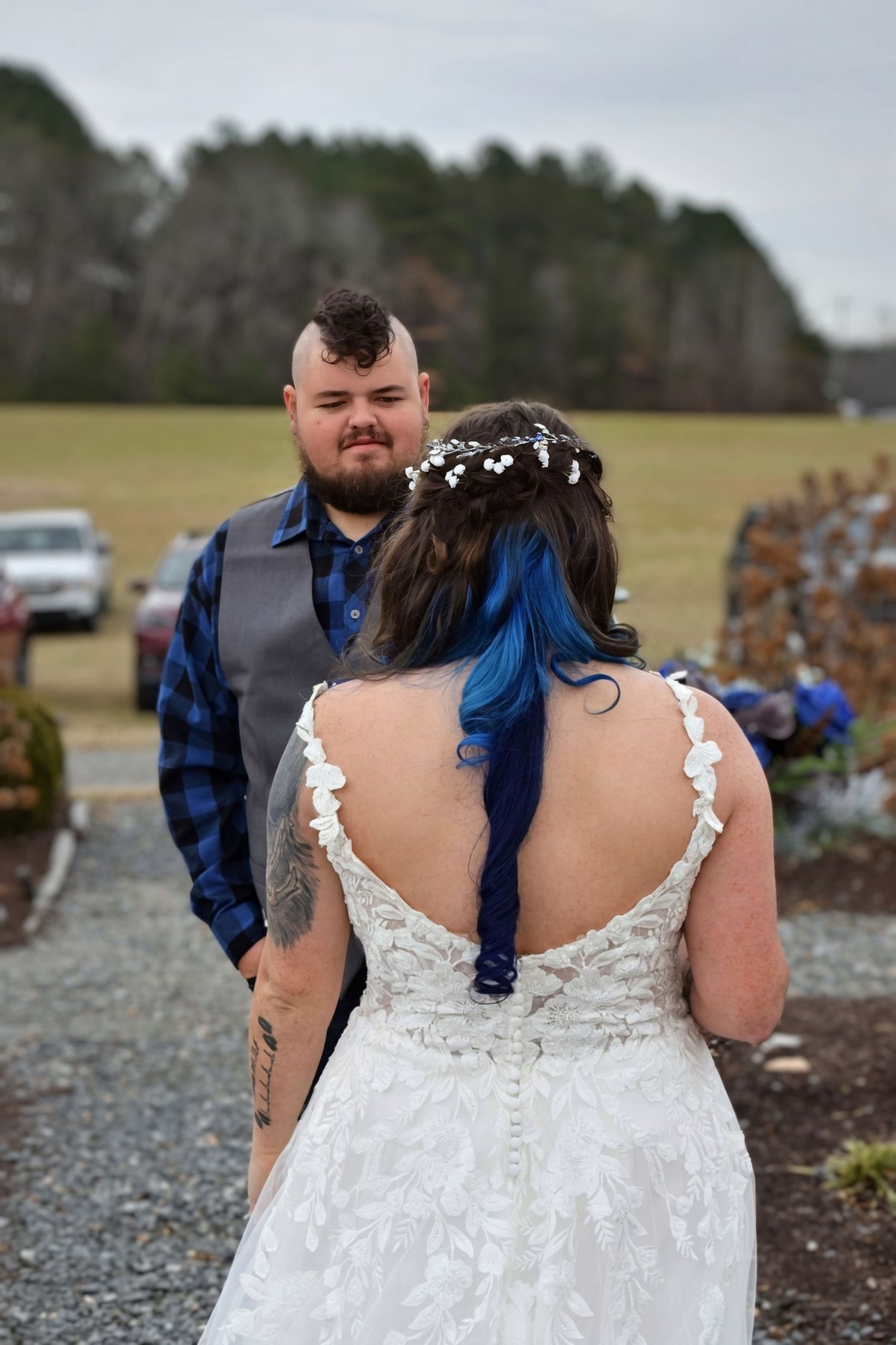 Groom emotional during outdoor first look as bride in backless lace dress with blue hair approaches.