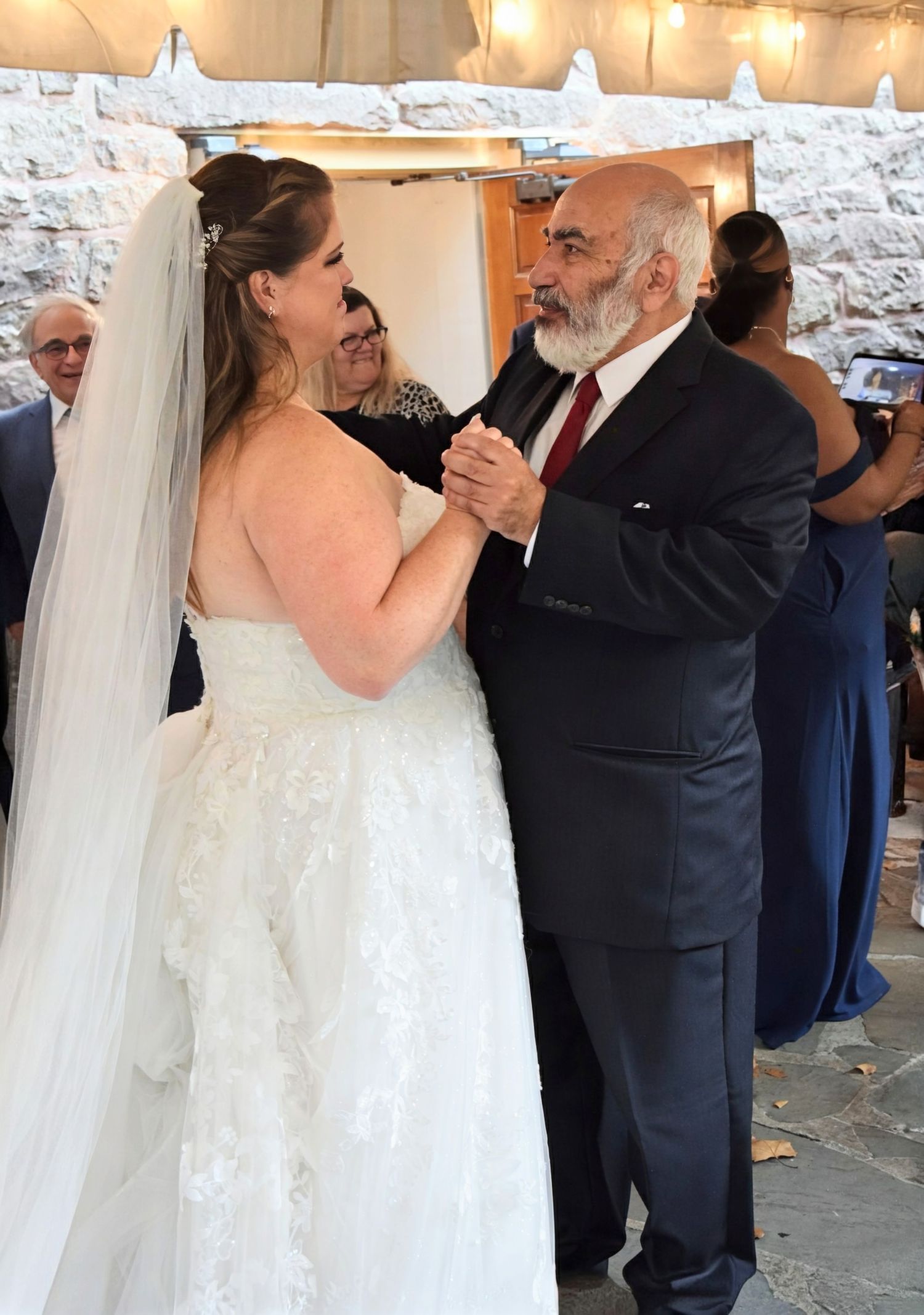 Bride in white lace wedding dress sharing father-daughter dance at elegant wedding reception.