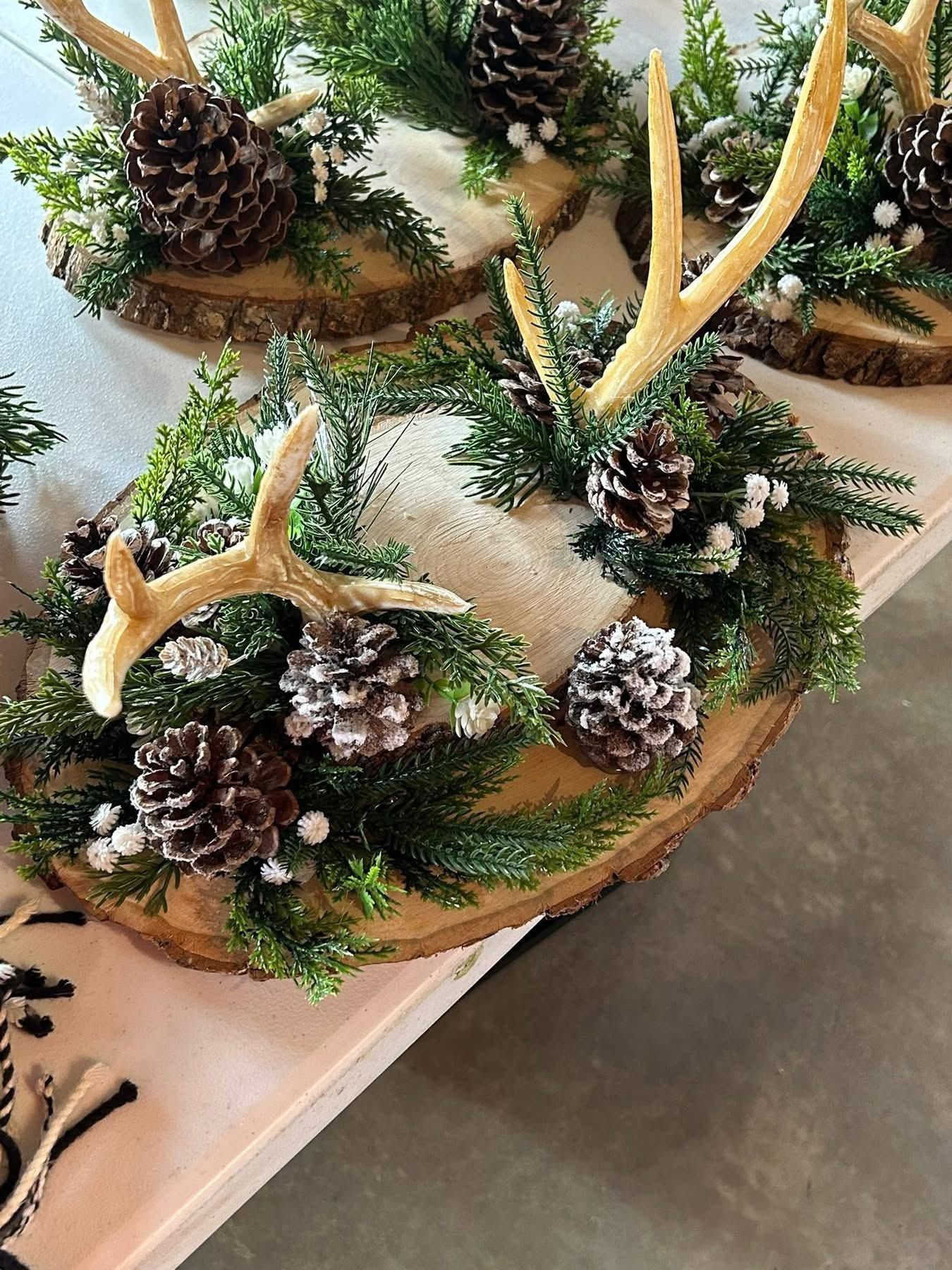 Rustic holiday centerpieces featuring deer antlers, frosted pine cones, and greenery on wood slices.