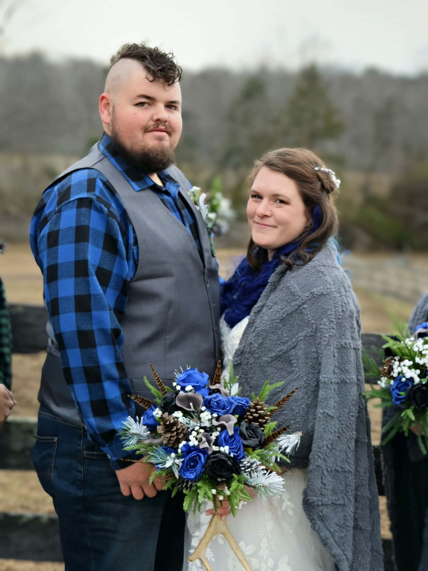 Wedding couple posing outdoors in winter, groom in blue plaid shirt, bride holding blue and white bouquet.