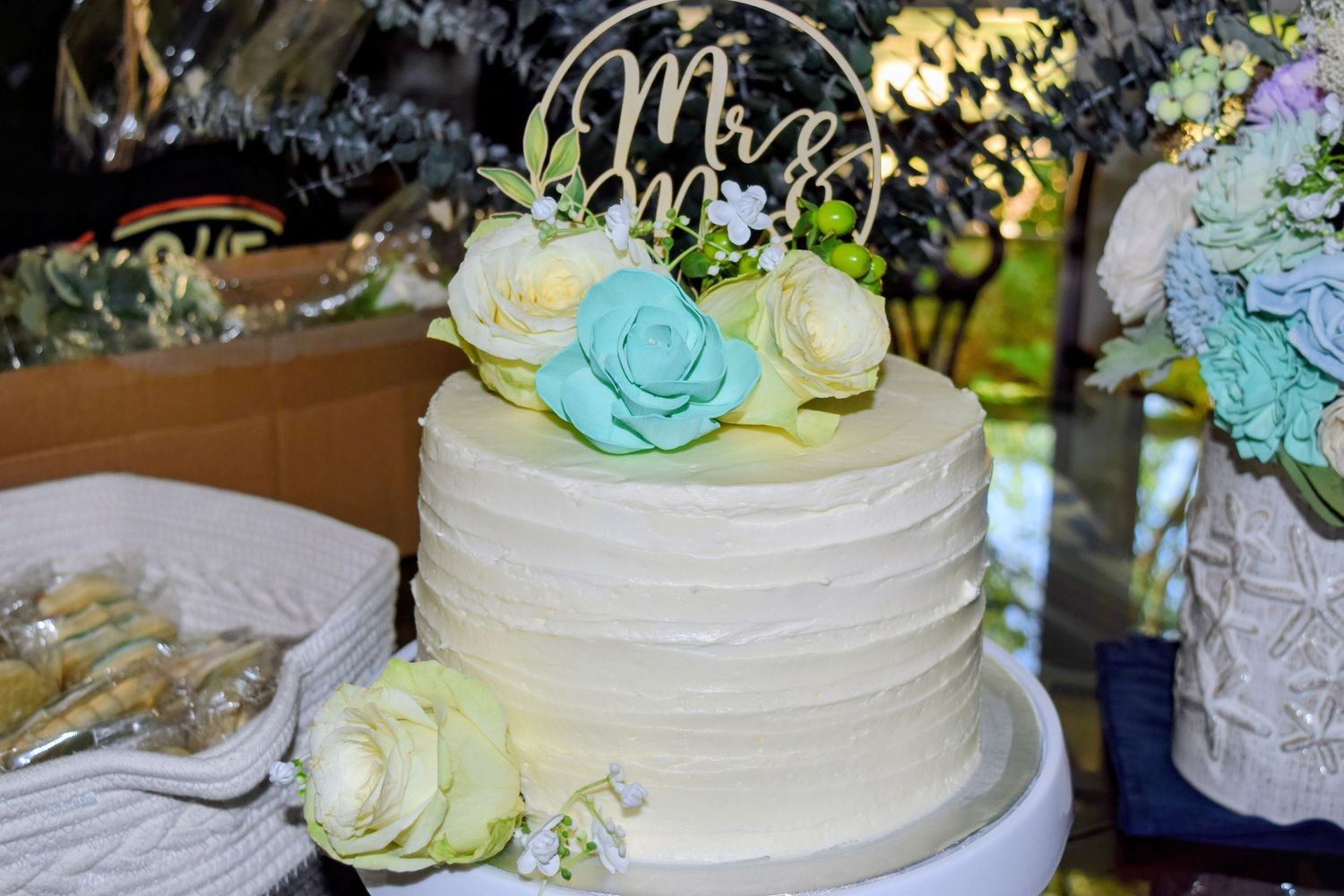 Elegant white wedding cake with teal and ivory floral decorations and a Mr. and Mrs. gold cake topper.
