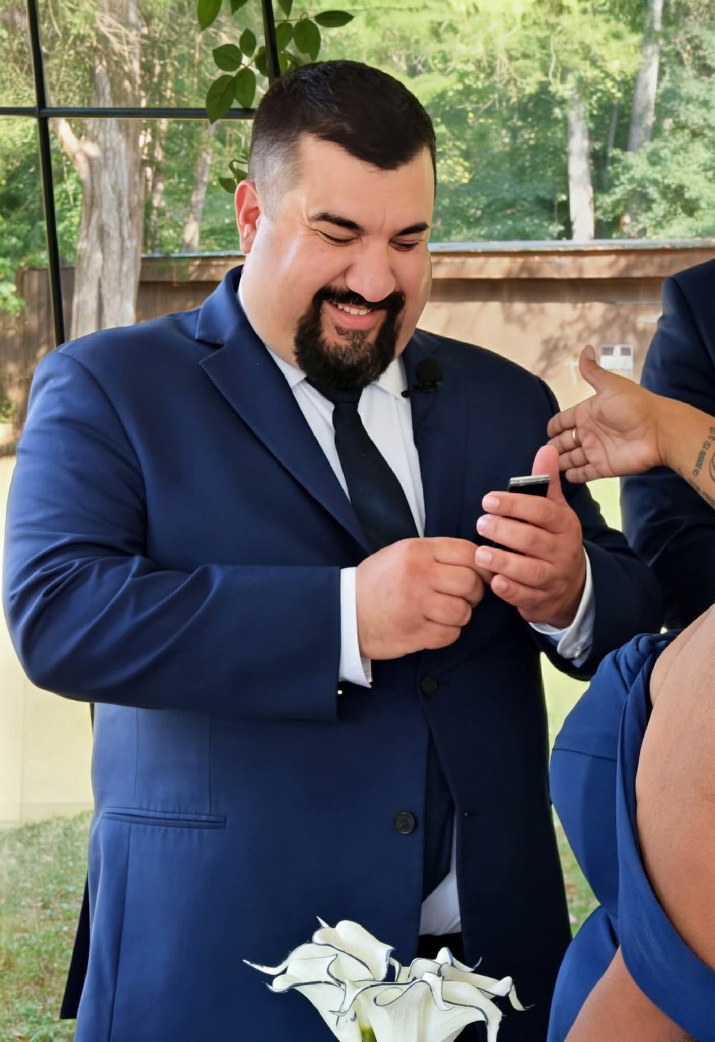 Smiling groom in navy blue suit examining wedding ring during ceremony.
