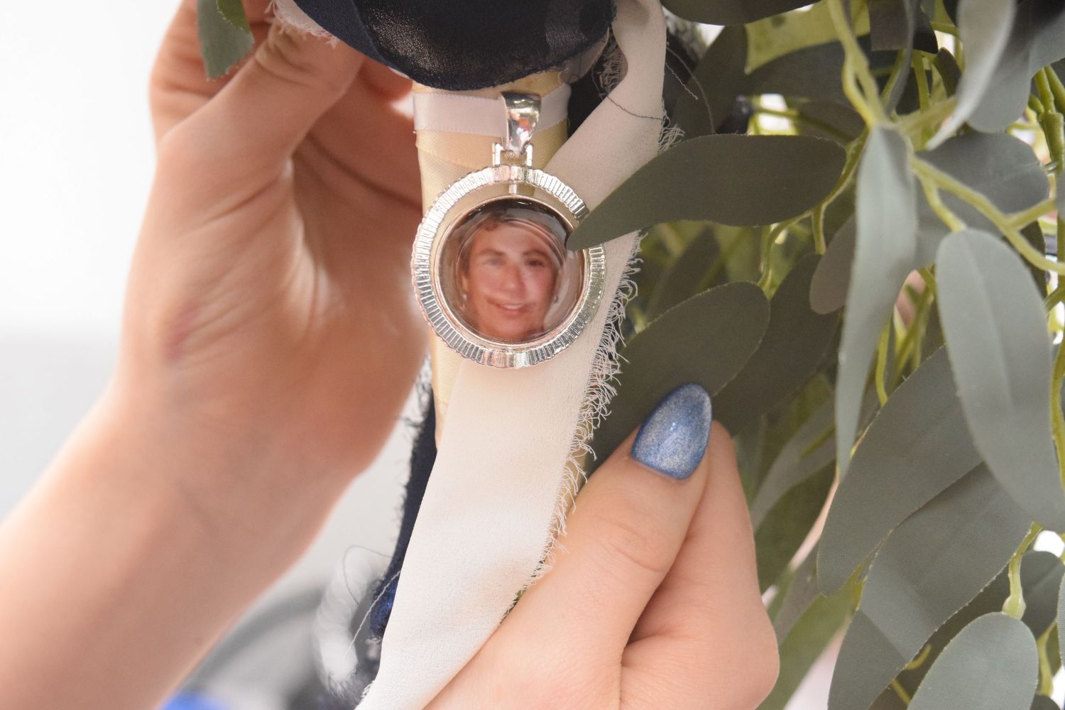 Hand holding a round locket charm containing a small portrait photo, attached to a wedding bouquet ribbon.