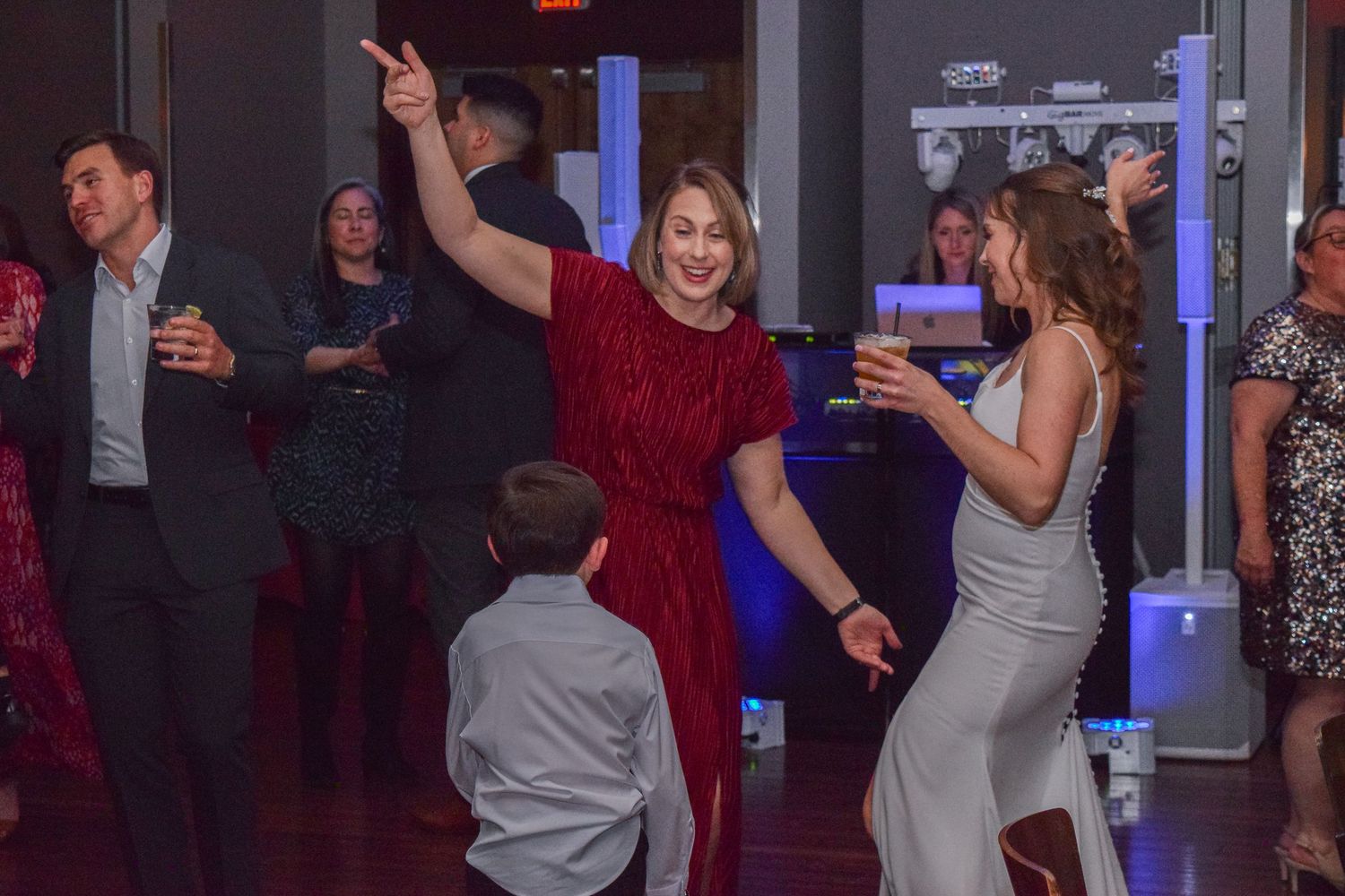 Guests dancing joyfully at wedding reception with woman in red dress raising hand.